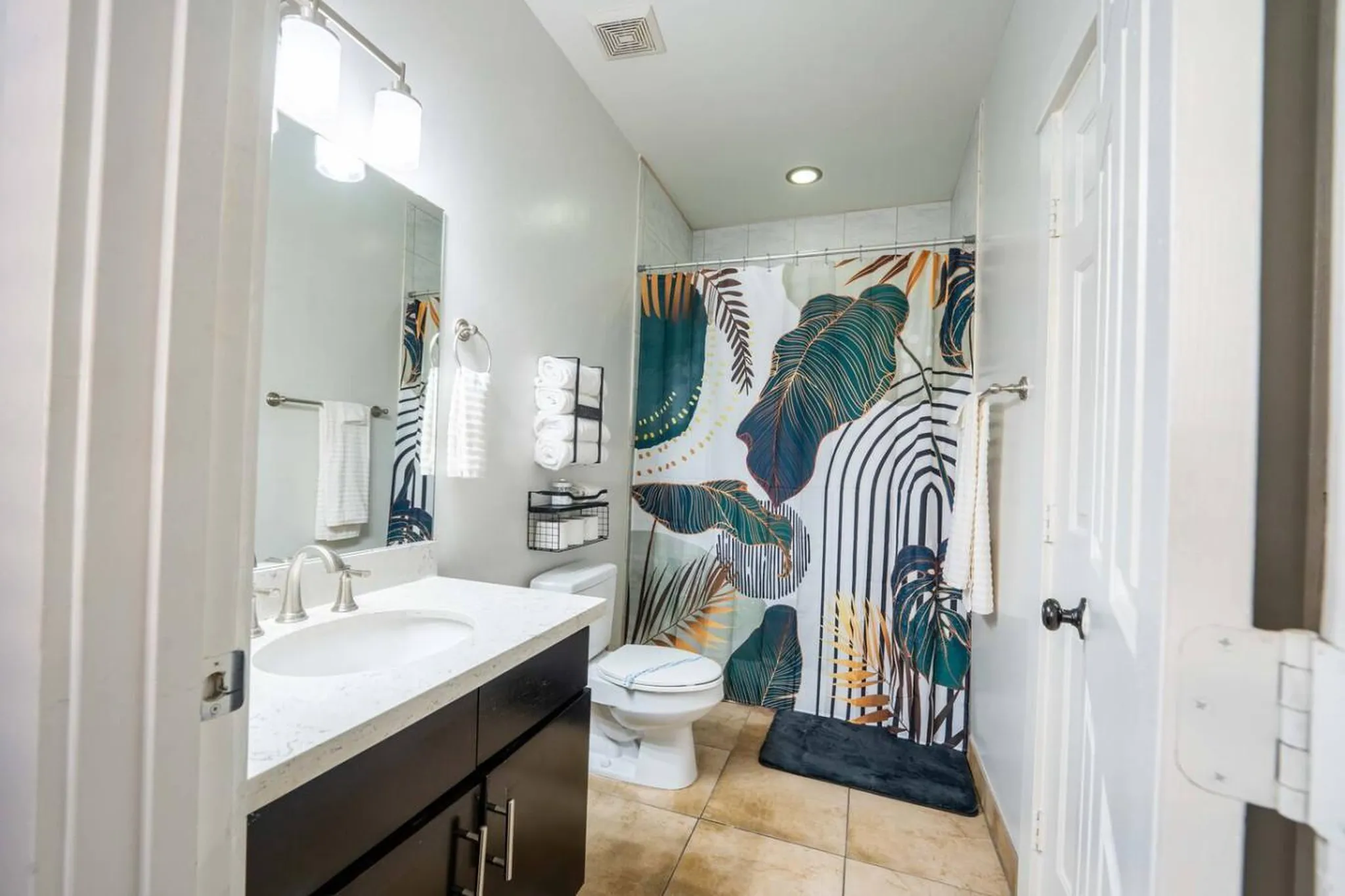 A modern bathroom with a dark wood vanity, white sink, and a tropical-themed shower curtain.