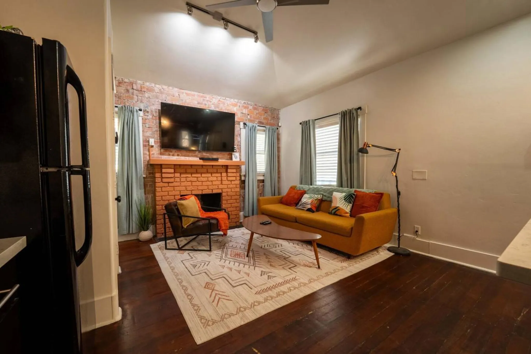 Living room with a yellow sofa, brick fireplace, TV, and a patterned rug.