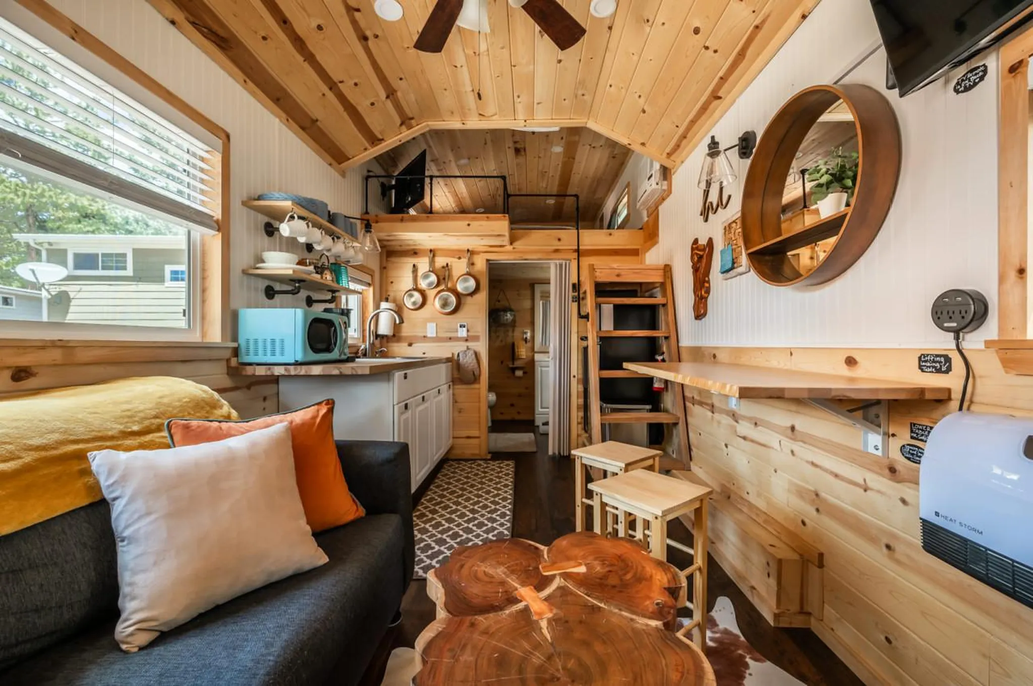 A cozy tiny house interior with a couch, kitchen, and loft.