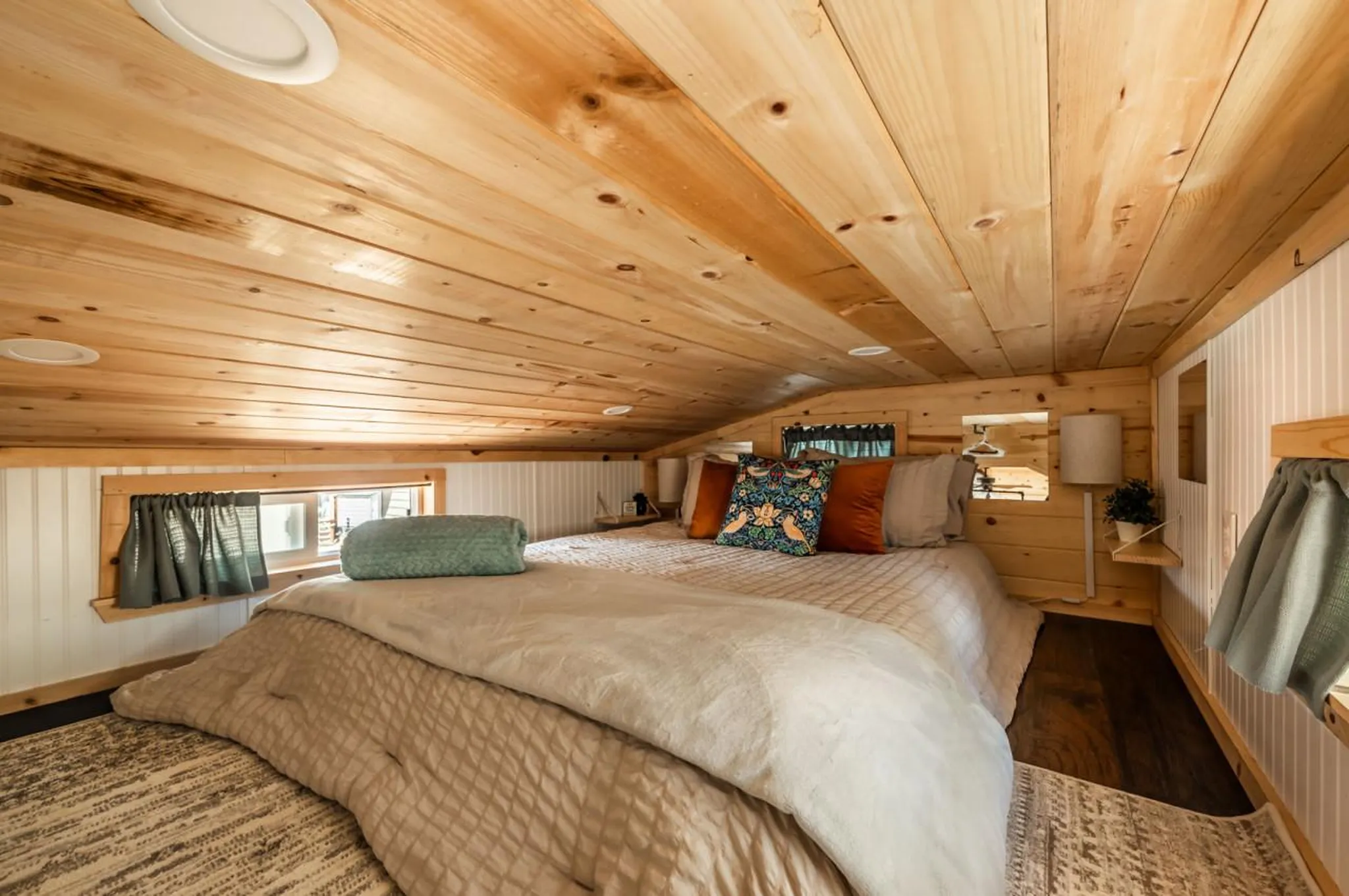 A cozy loft bedroom with a wooden ceiling and a bed with decorative pillows.