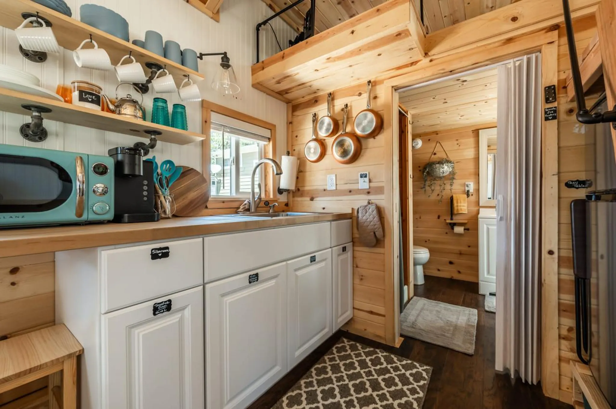 Kitchen and bathroom interior of a tiny house with wooden walls and cabinets.