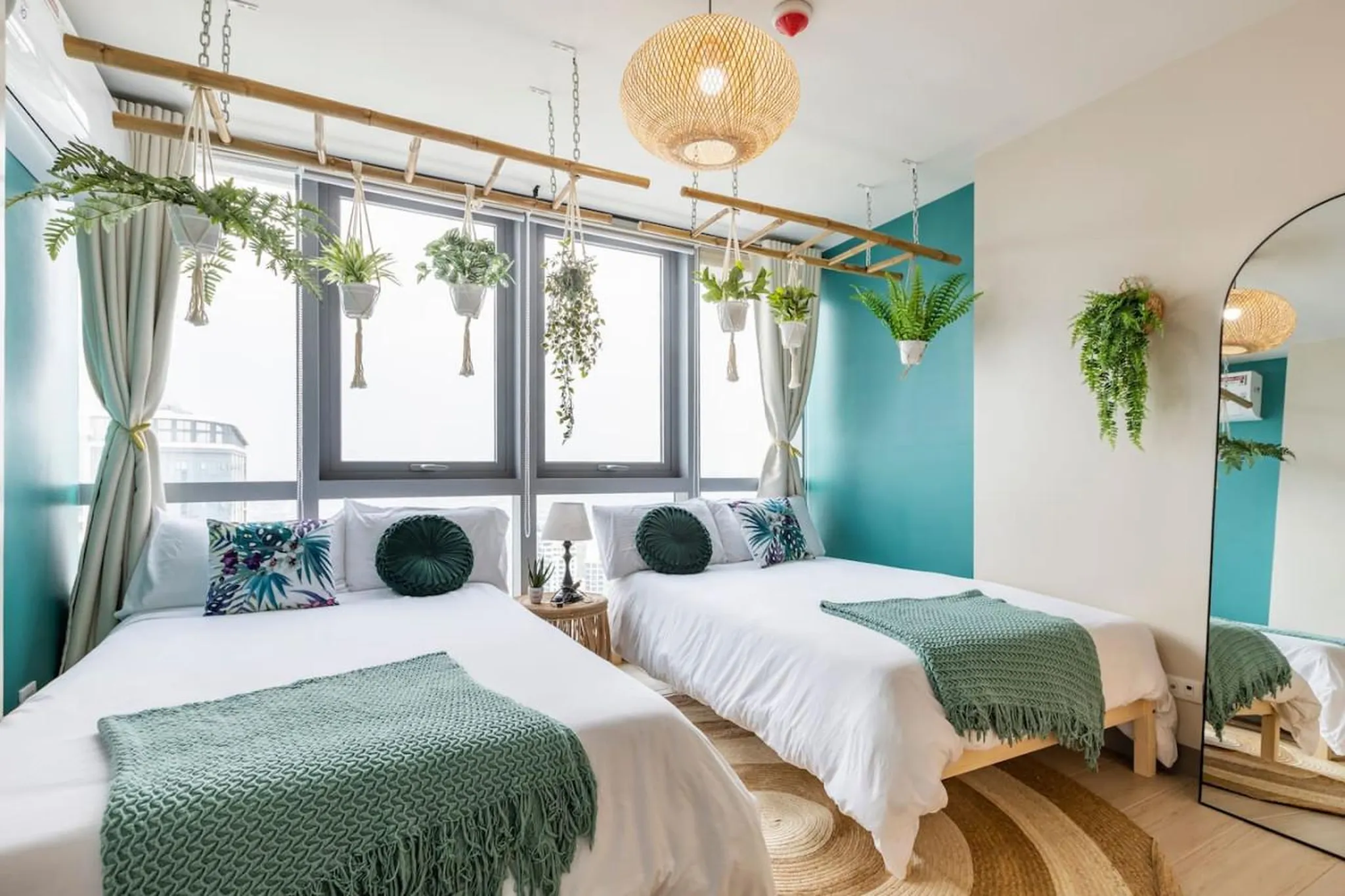 A modern bedroom with two beds, lush hanging plants, and a tropical accent pillow.