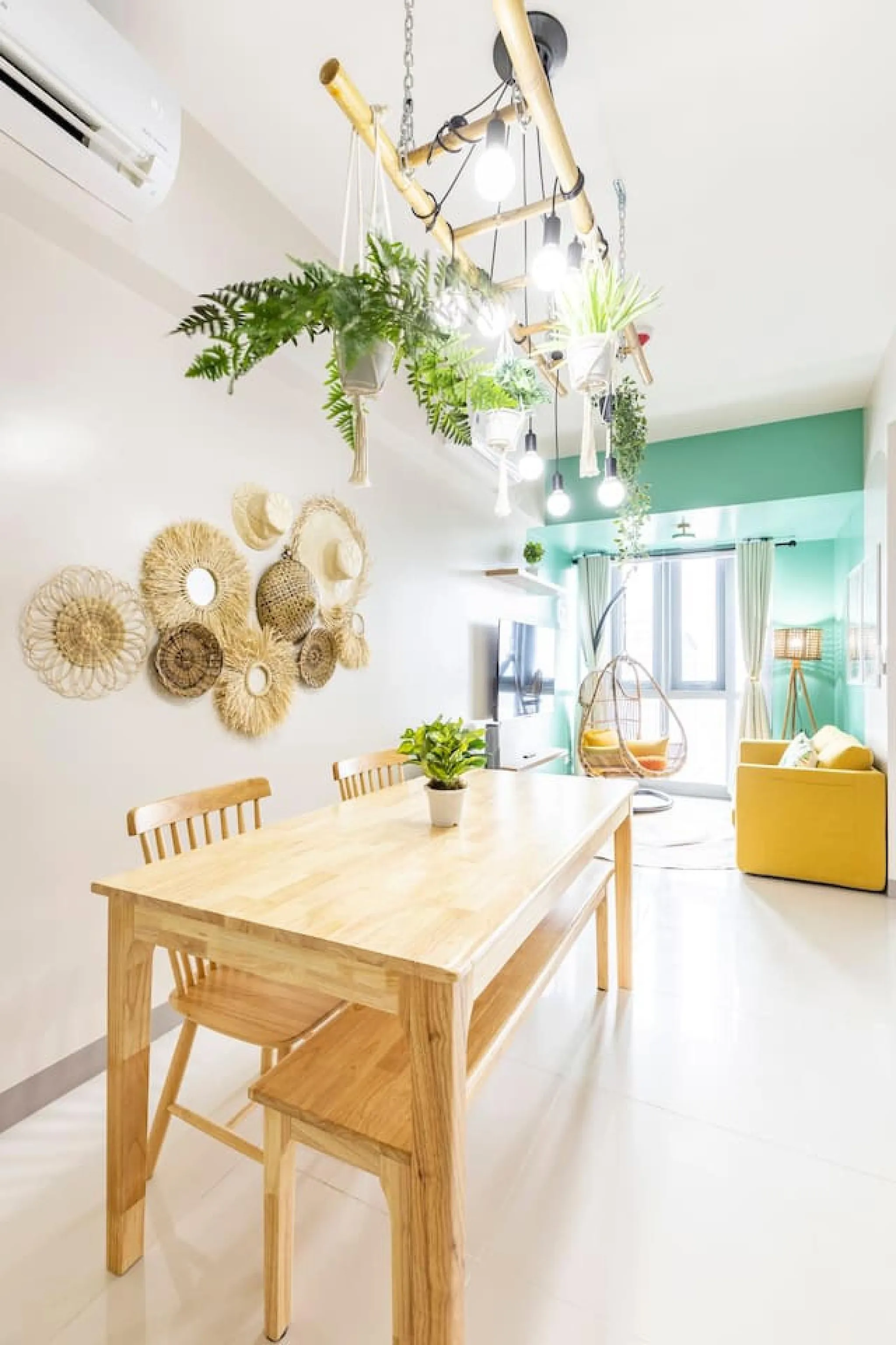 A dining table and chairs are in the foreground, with hanging plants and a yellow couch in the backg