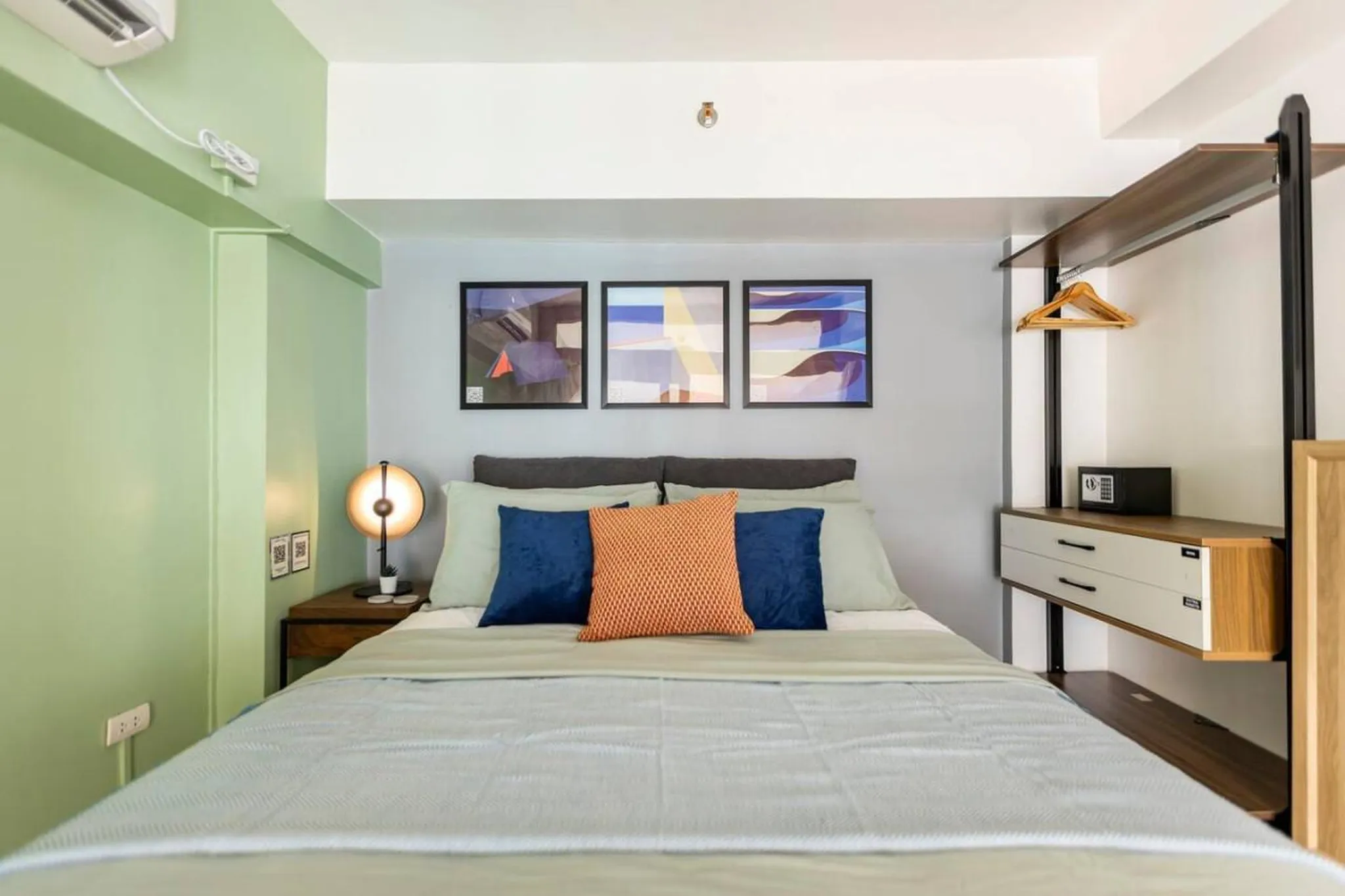 A minimalist bedroom with a bed, artwork, and a wardrobe.