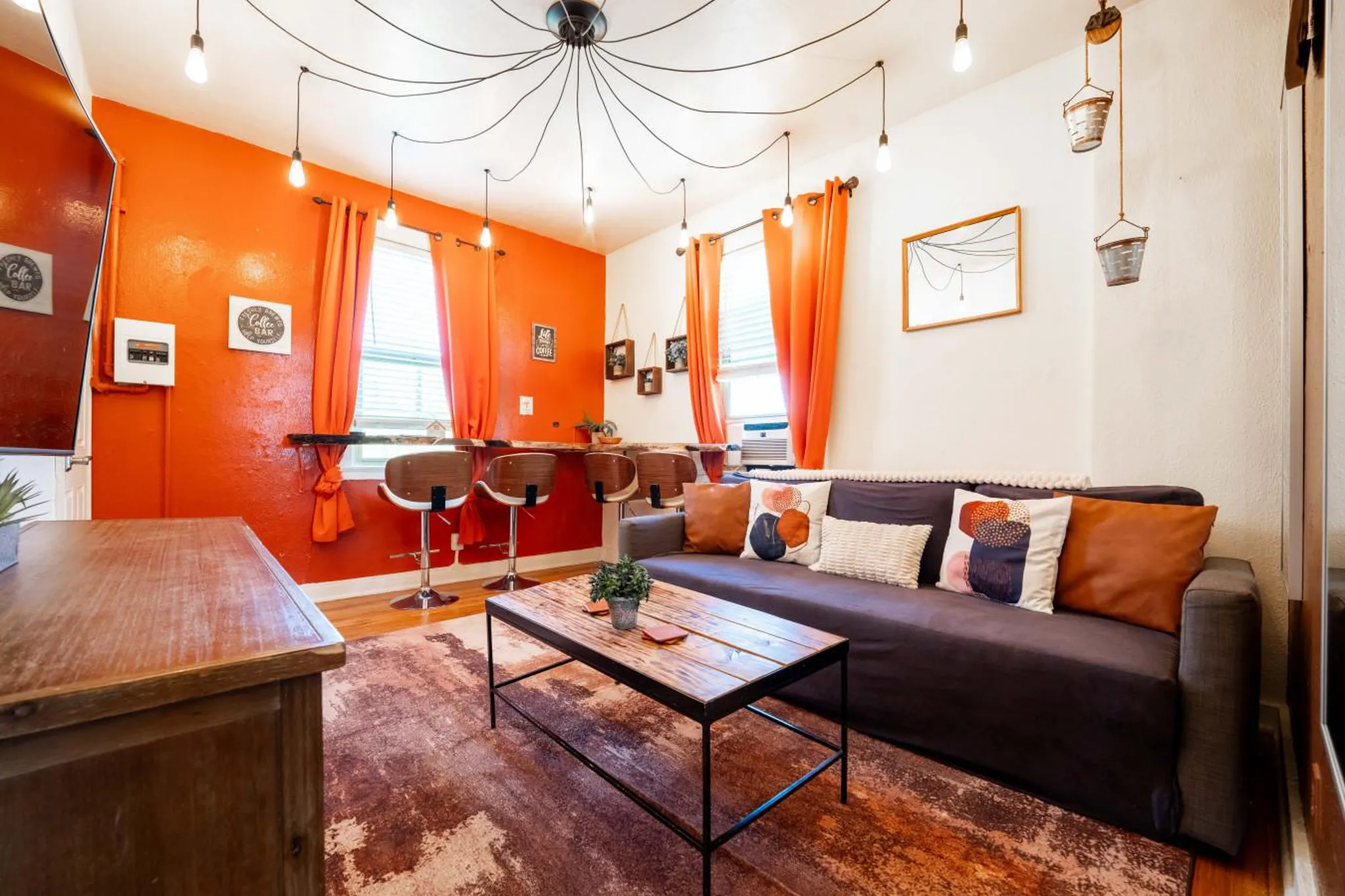 Modern living room with orange walls, a sofa, coffee table, and bar stools.