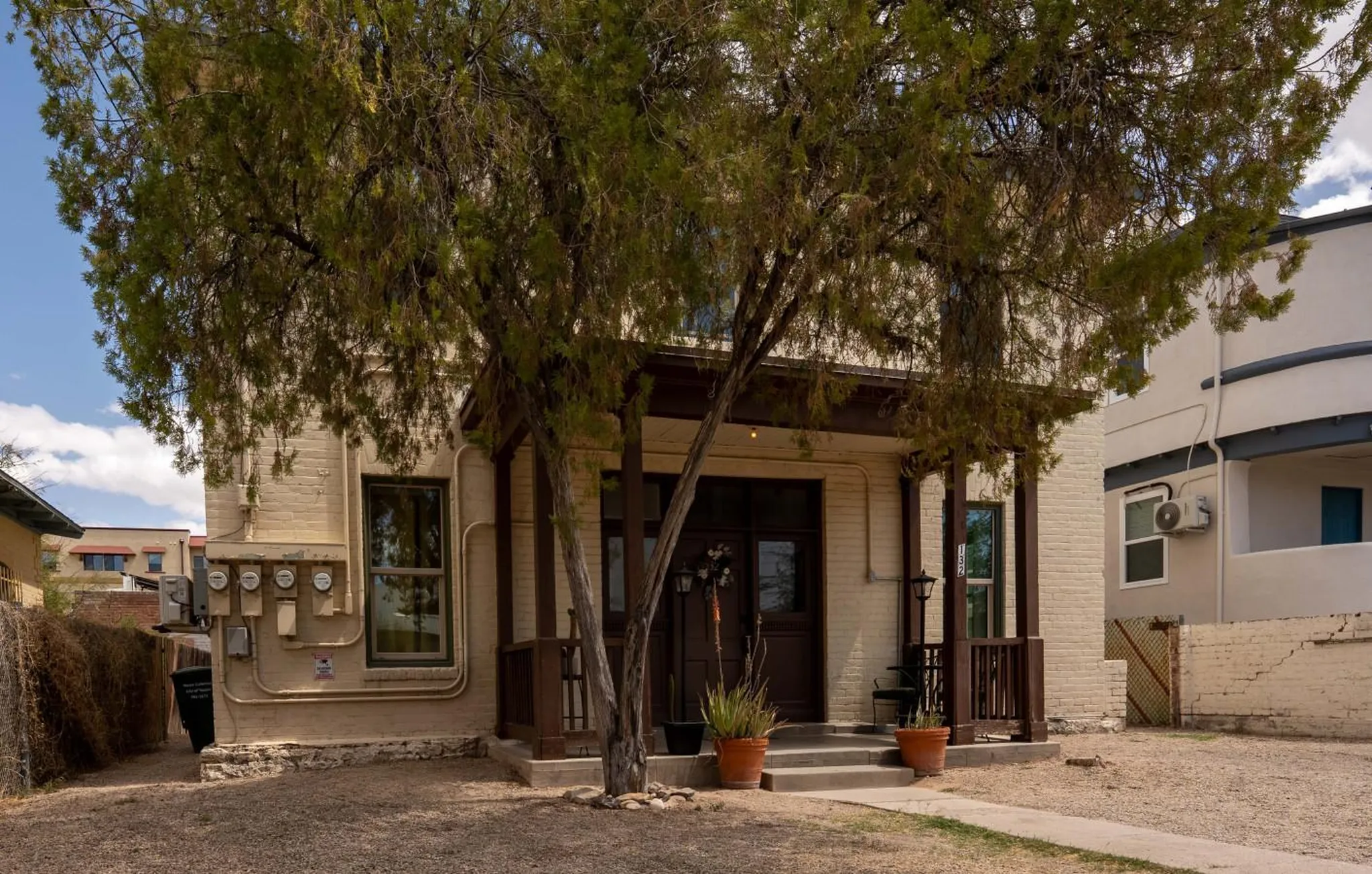 A front view of a beige brick building with a porch and trees in front.