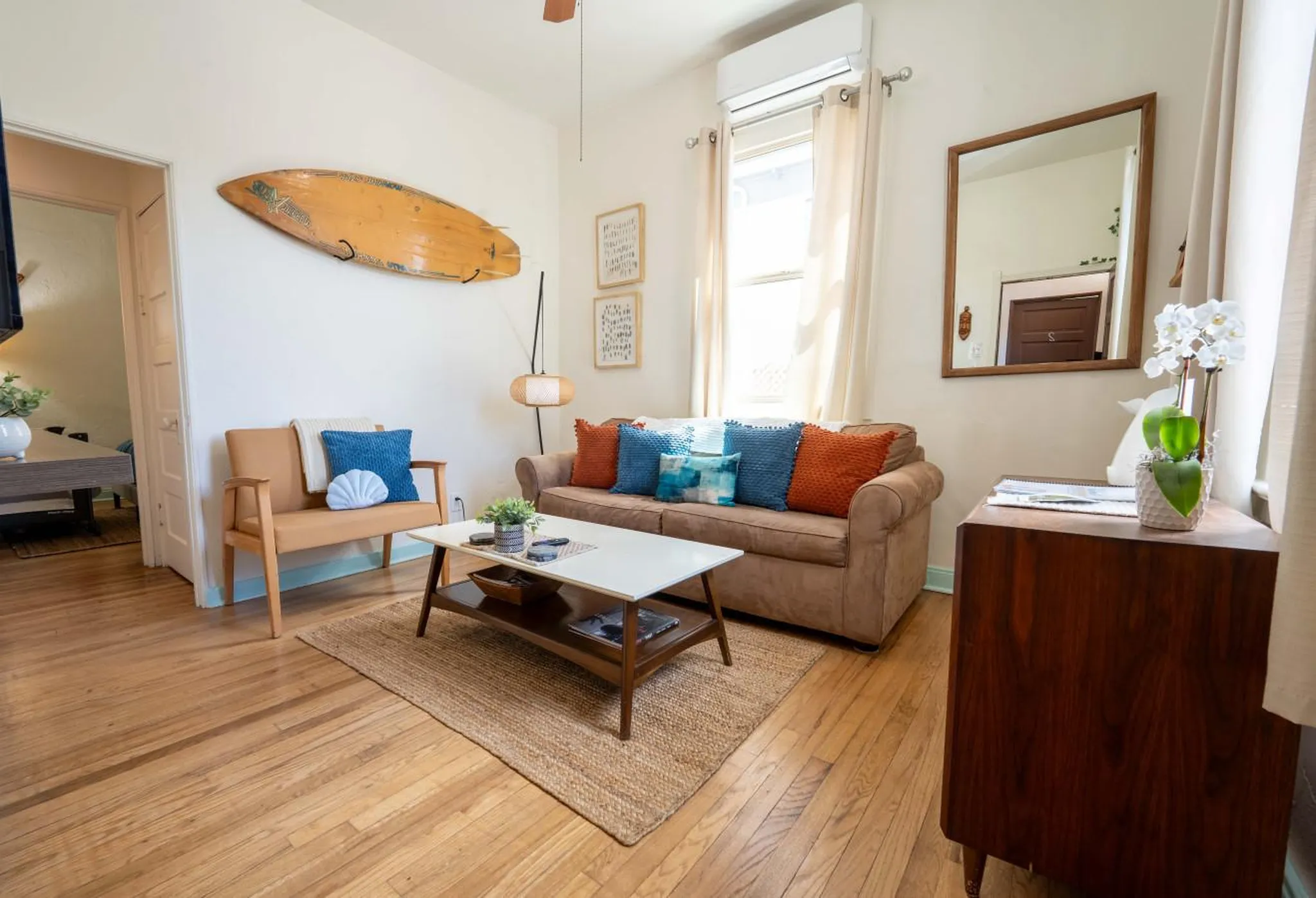 A living room with a brown couch, a tan armchair, and a surfboard on the wall.