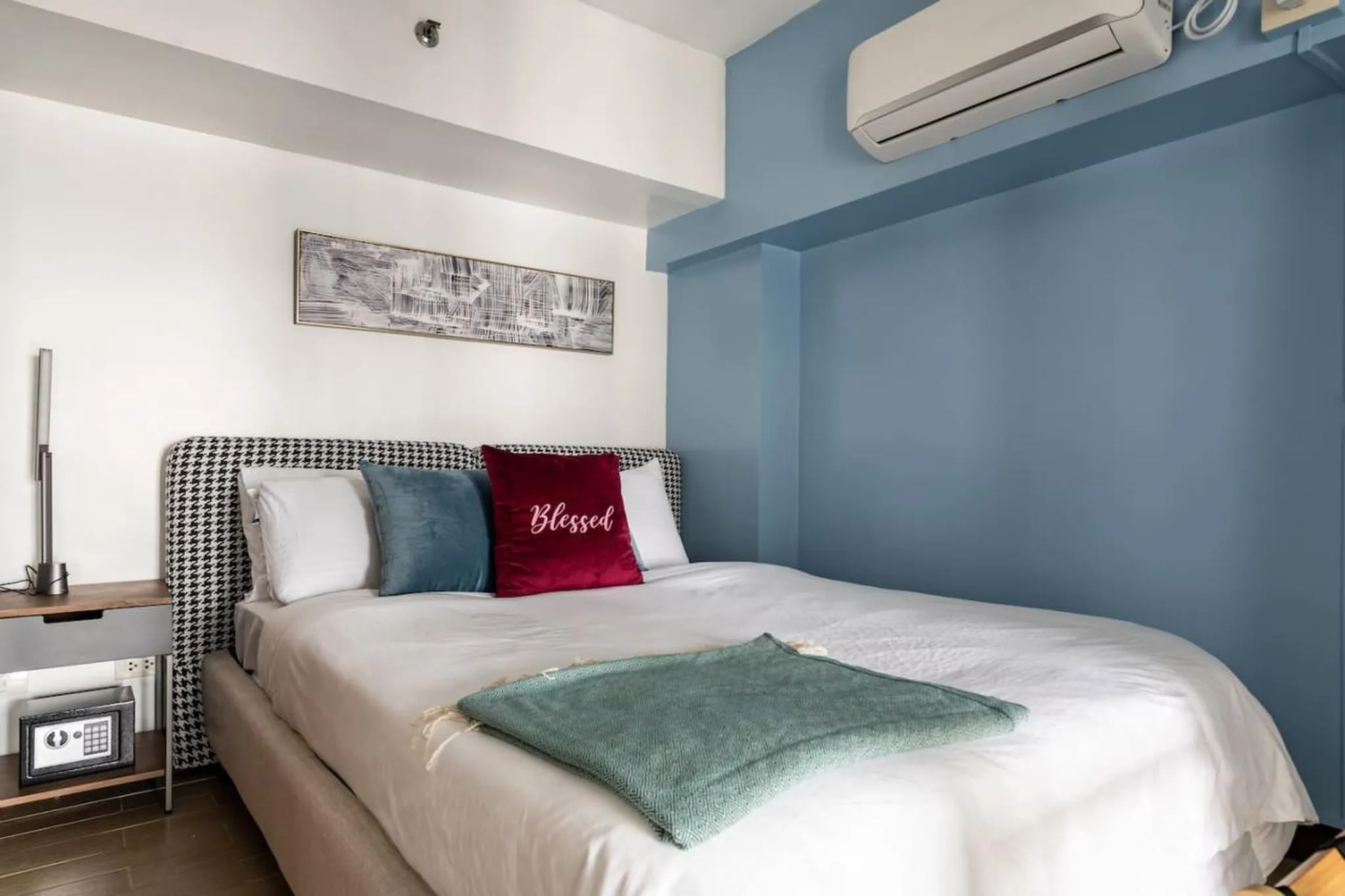 A modern bedroom with a blue wall, air conditioner, and a dogtooth headboard.
