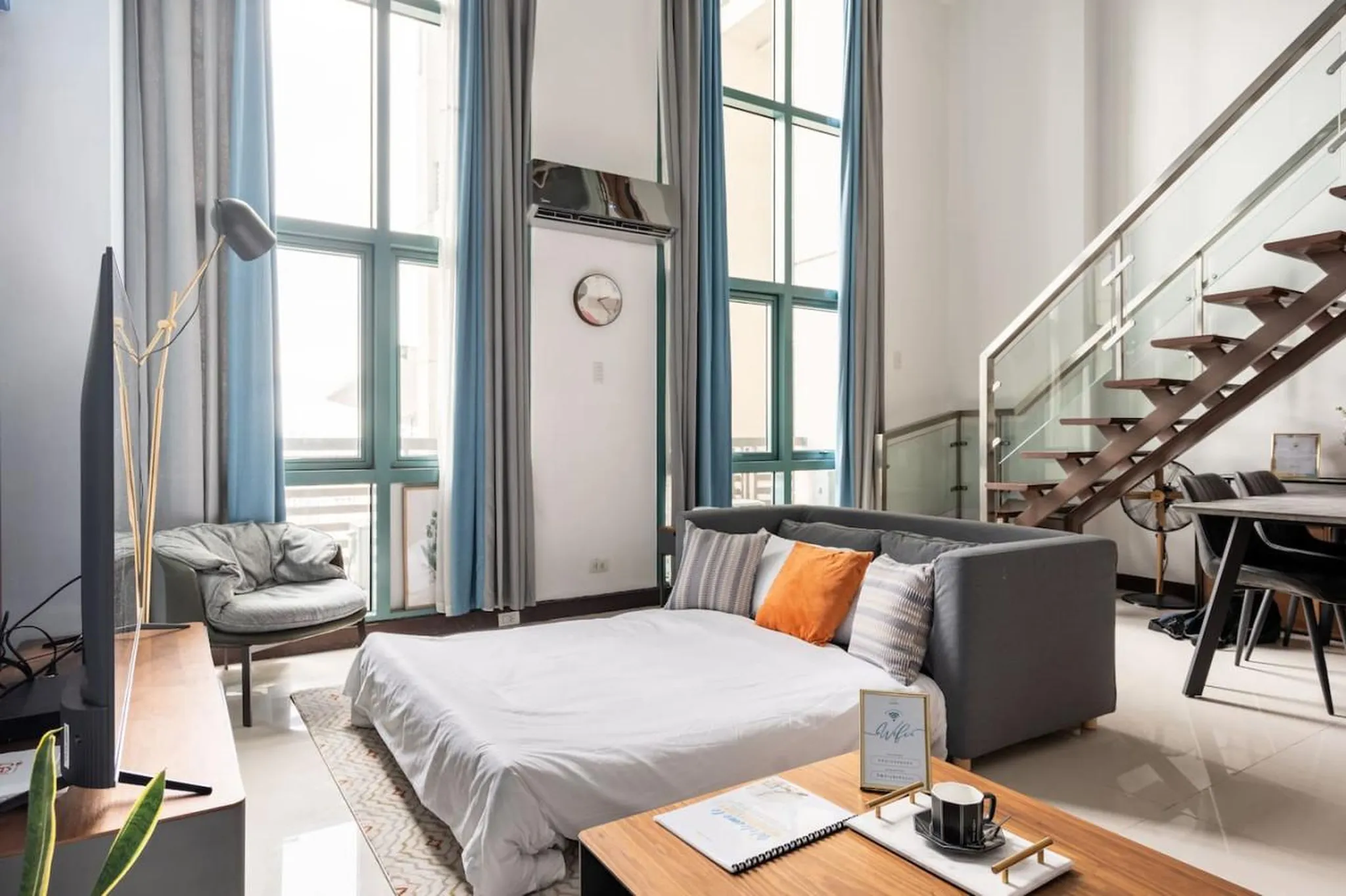 A modern living room with a bed, sofa, and stairs.