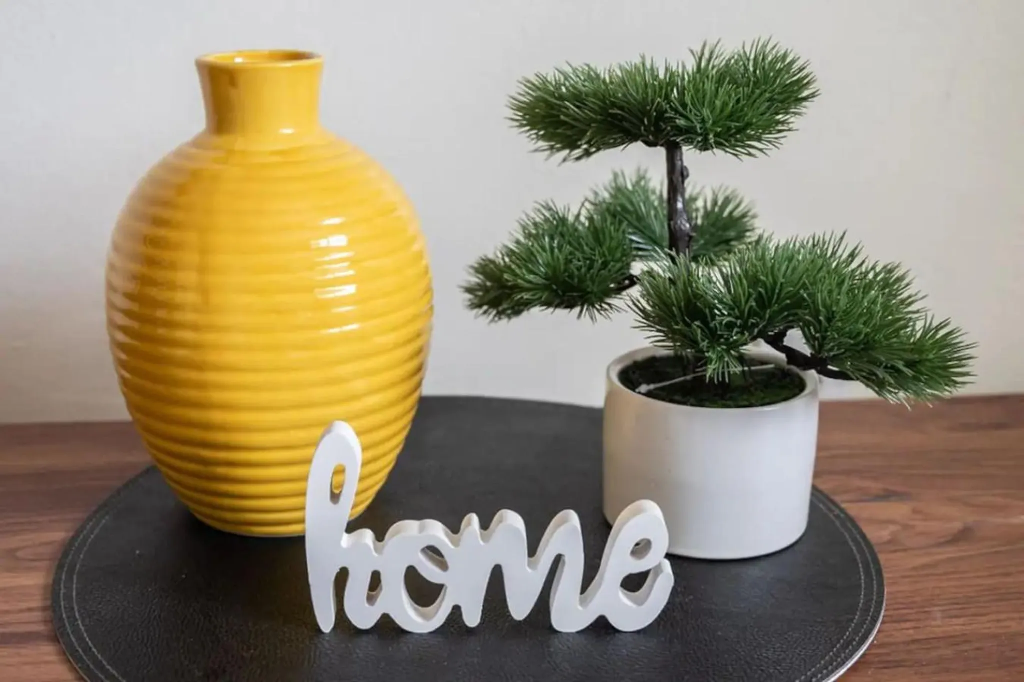 A yellow vase, a bonsai tree, and a white "home" sign sit on a dark placemat.