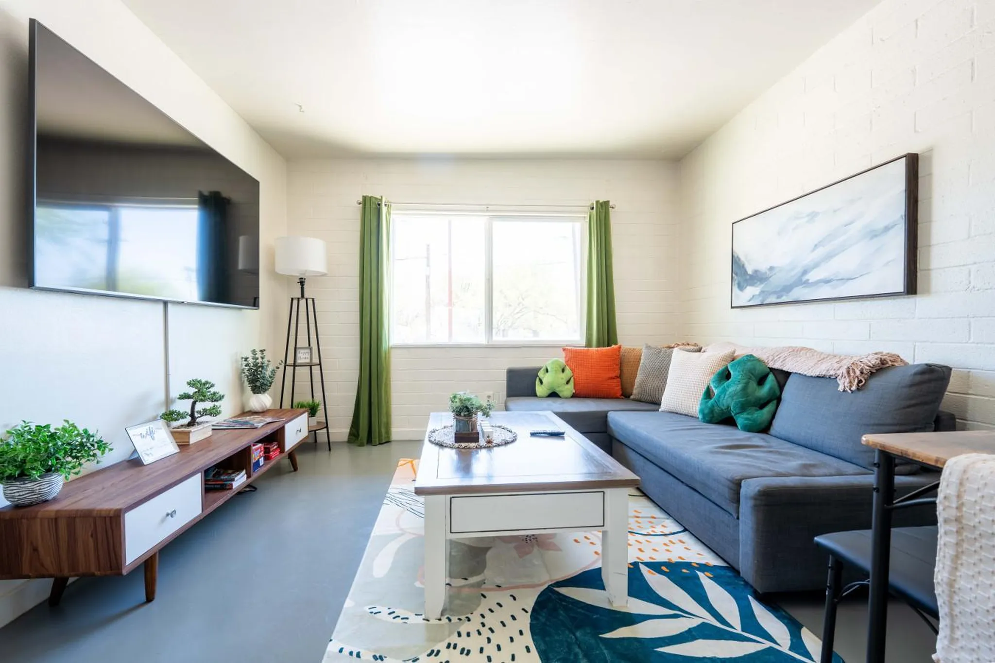 A modern living room with a grey sectional, colorful pillows, and a large flat-screen TV.