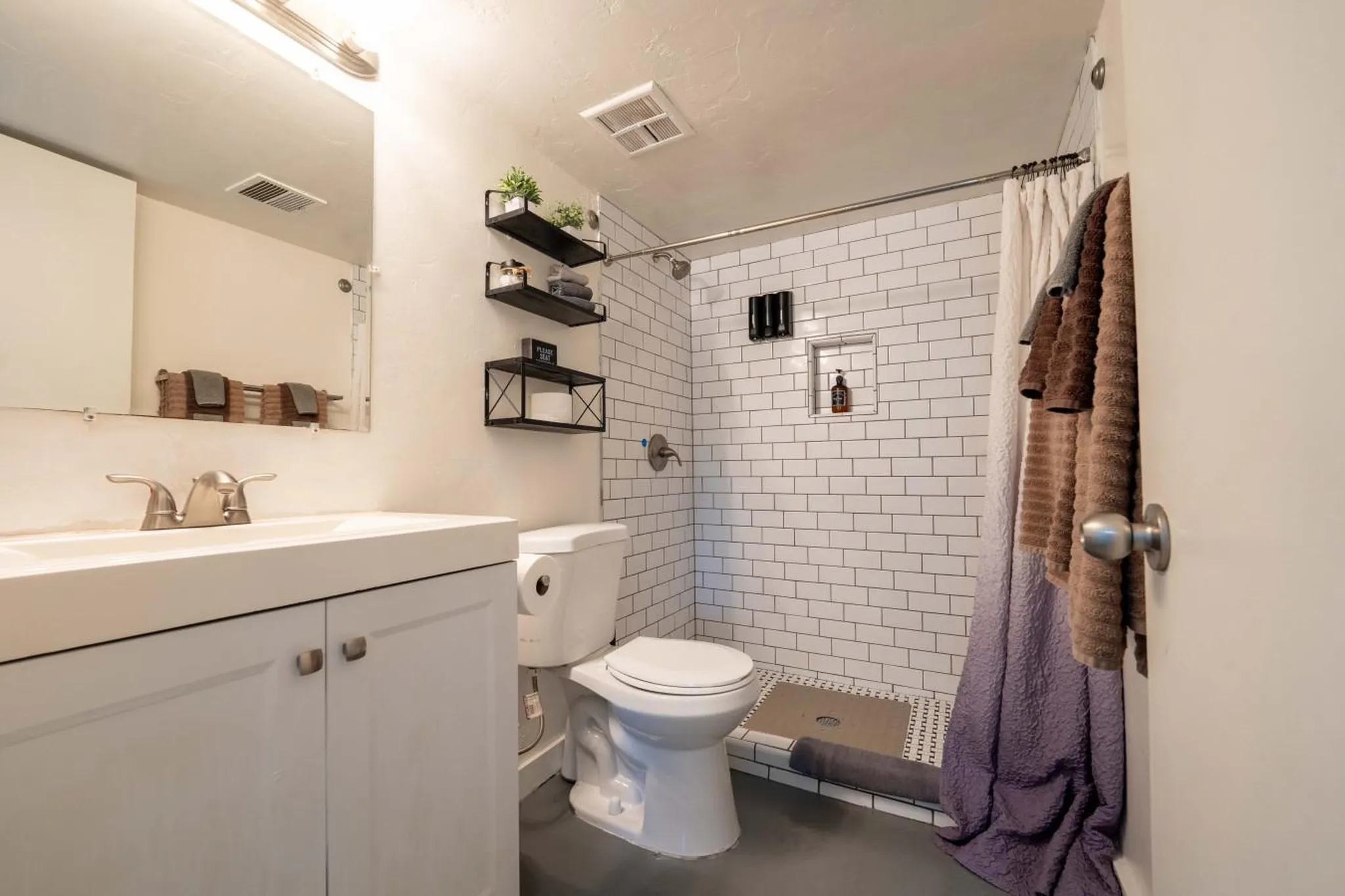 A clean and modern bathroom with a white vanity, toilet, and white tiled shower.