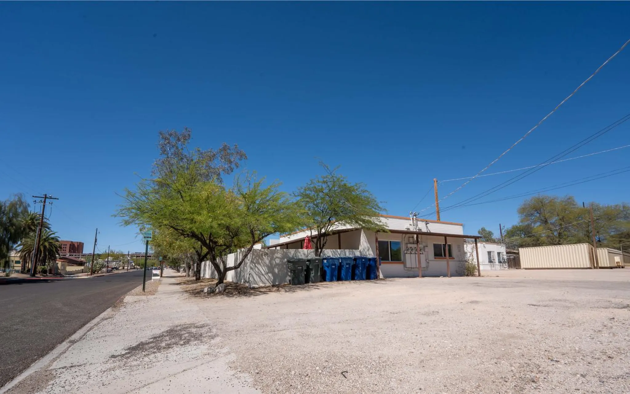 A low-angle shot of a small commercial building with trees and trash cans in front.