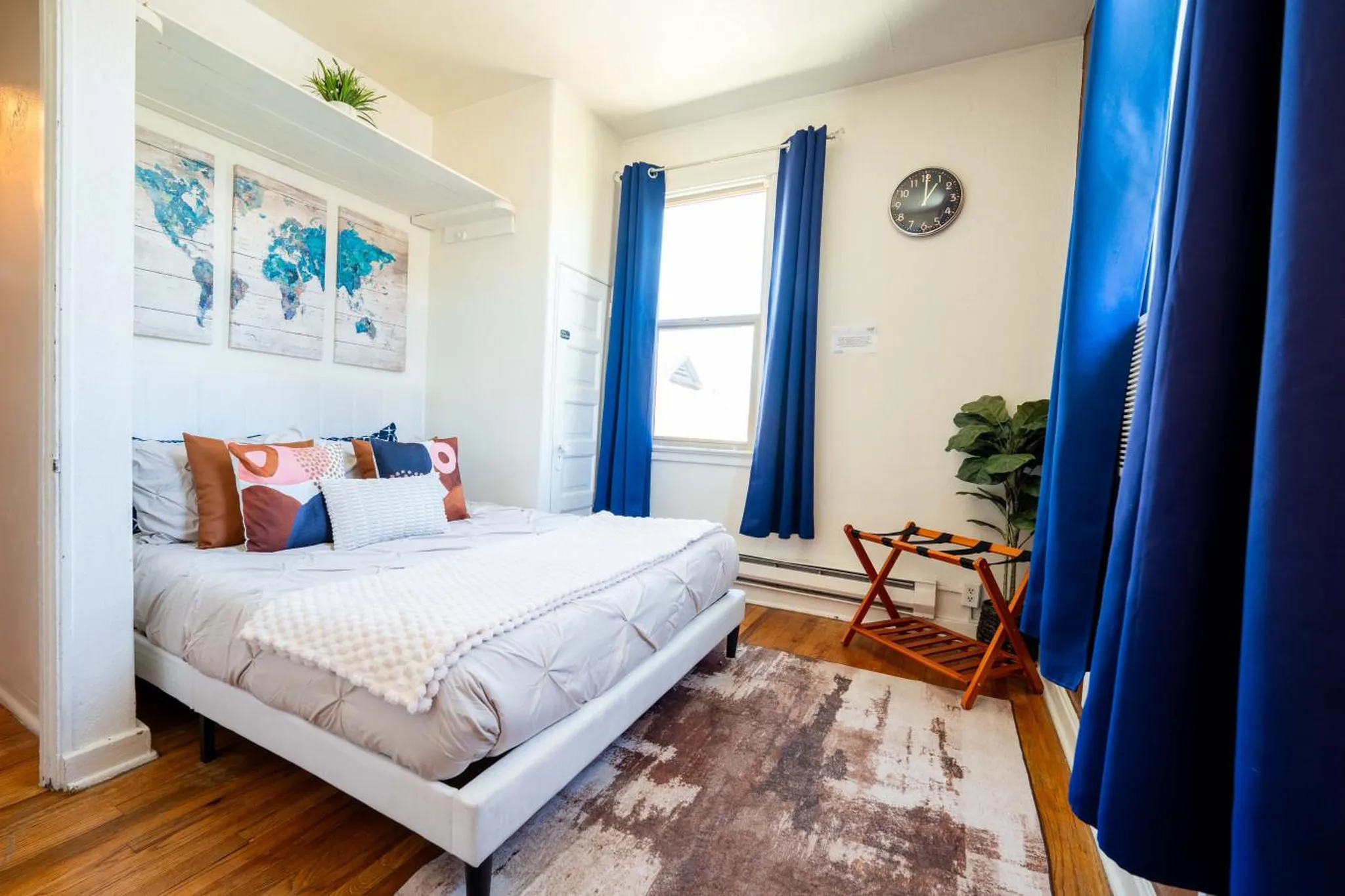 Bedroom with world map art, blue curtains, and a luggage rack.