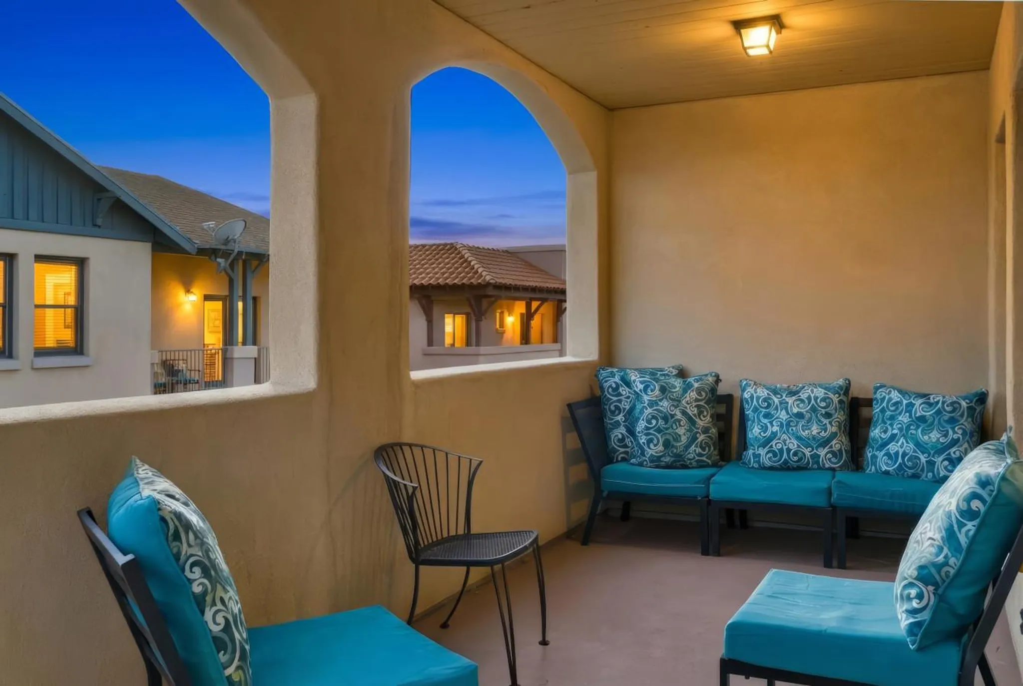Outdoor patio with arched openings, blue cushioned seating, and a small metal chair.
