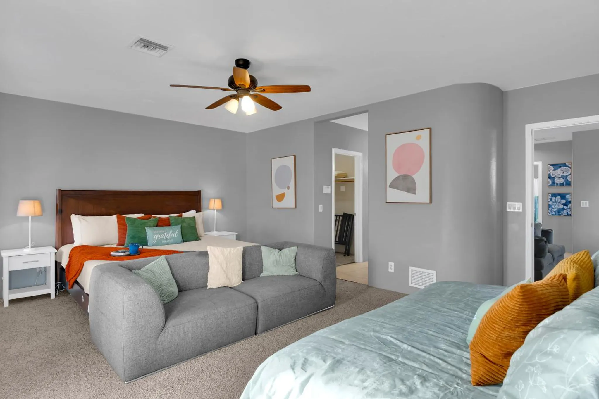 A contemporary bedroom with a grey couch, bed with pillows, and two framed abstract art pieces on th