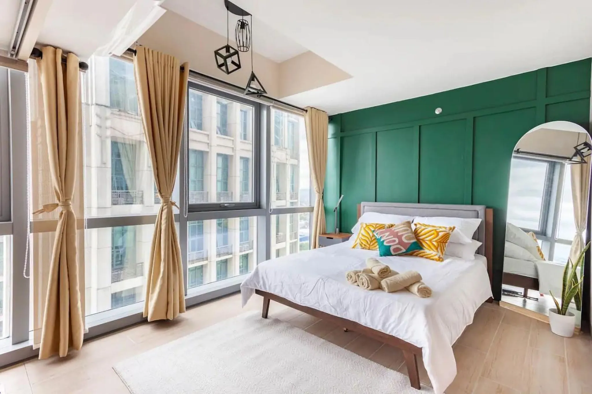 A modern bedroom with a king-size bed, green accent wall, and large windows.