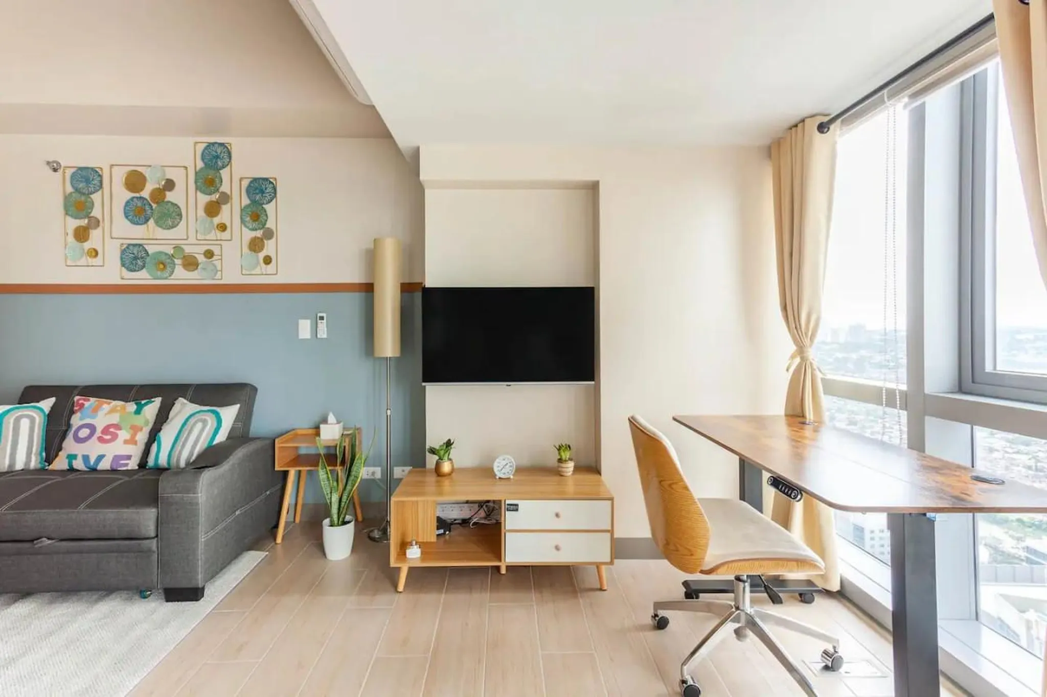 Modern living room with a sofa, TV, and a desk next to a window.