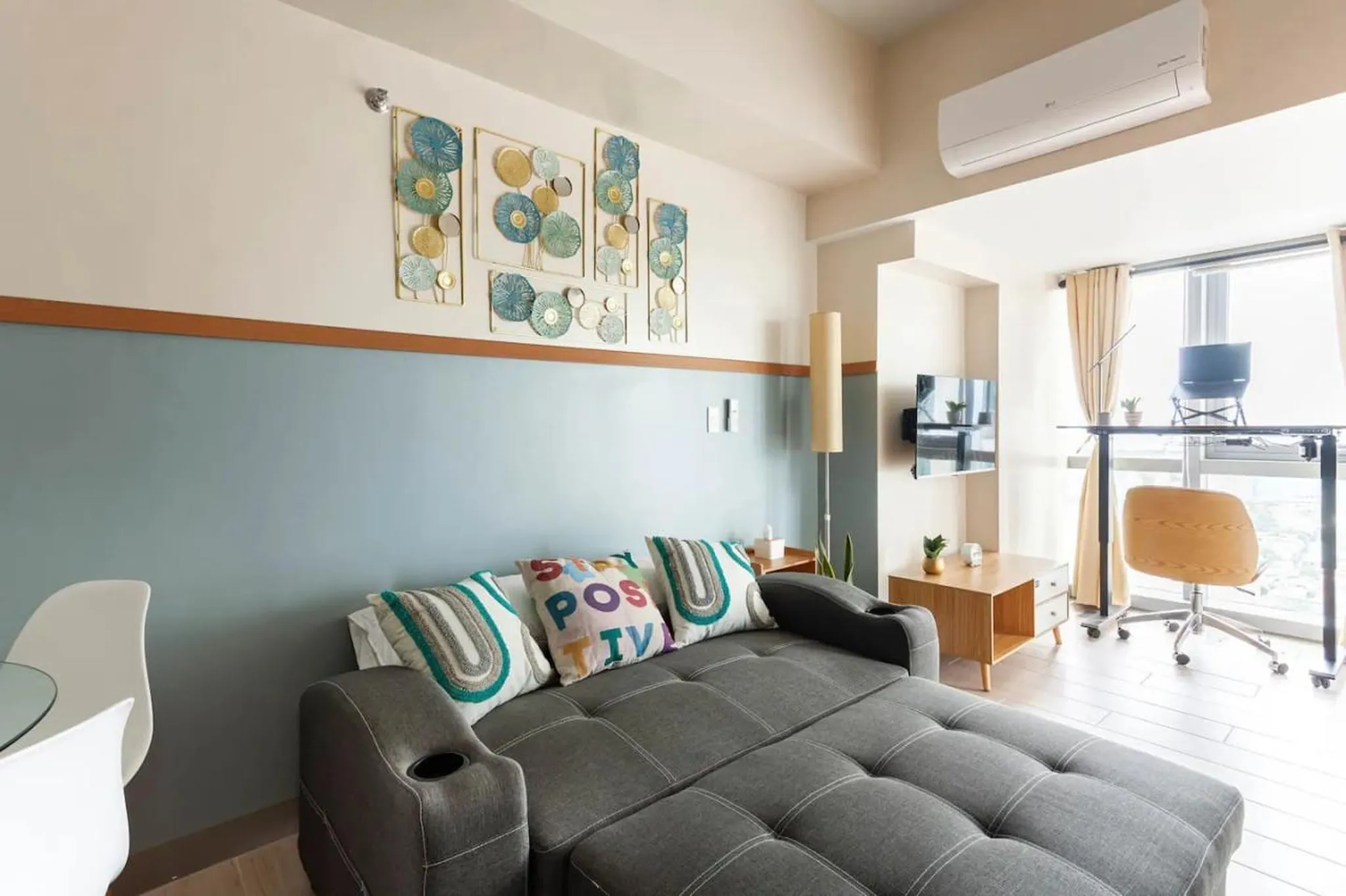 A sofa with decorative pillows faces a desk and chair by a window.