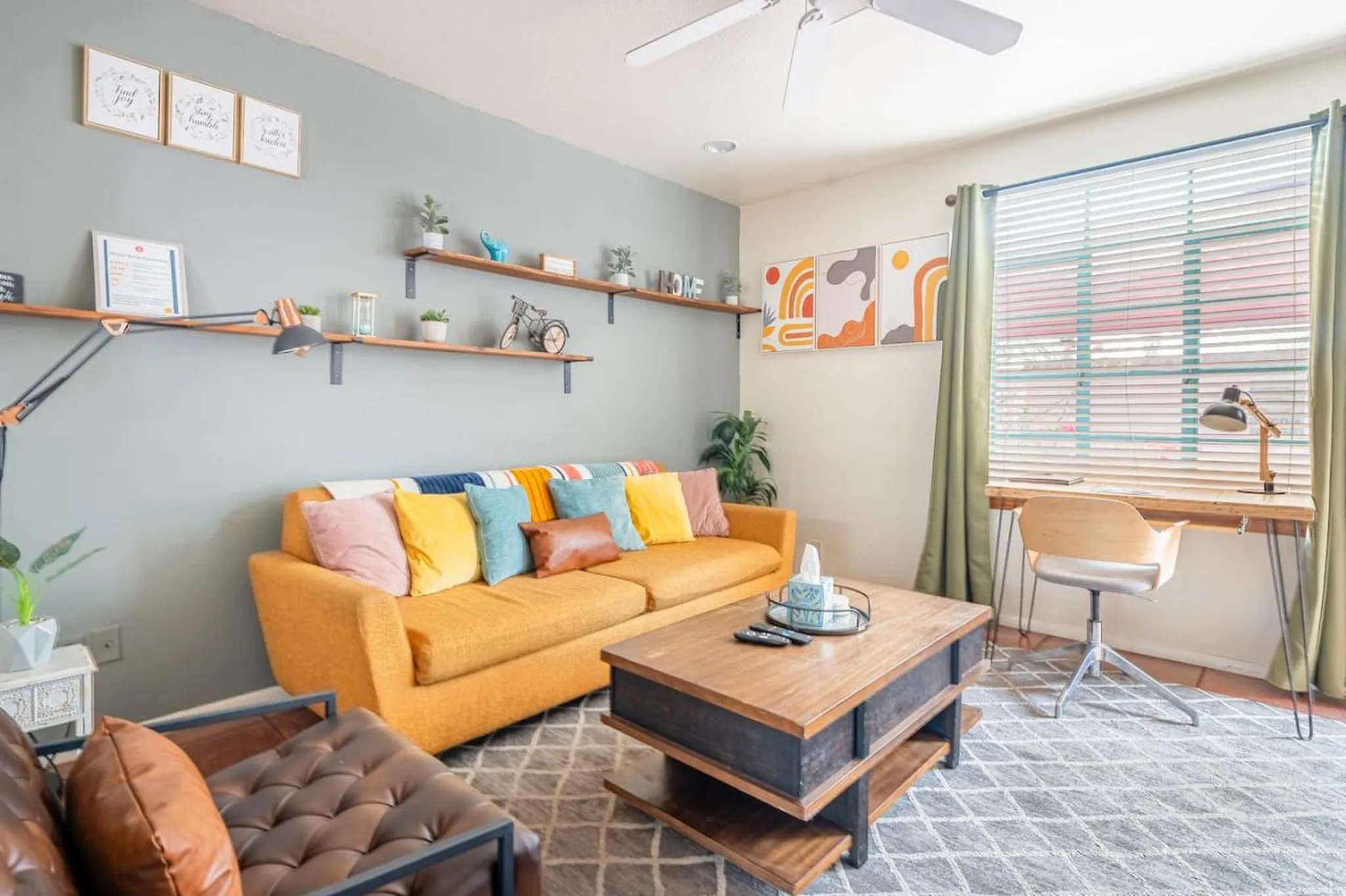 A living room with a yellow couch, coffee table, and a desk by the window.