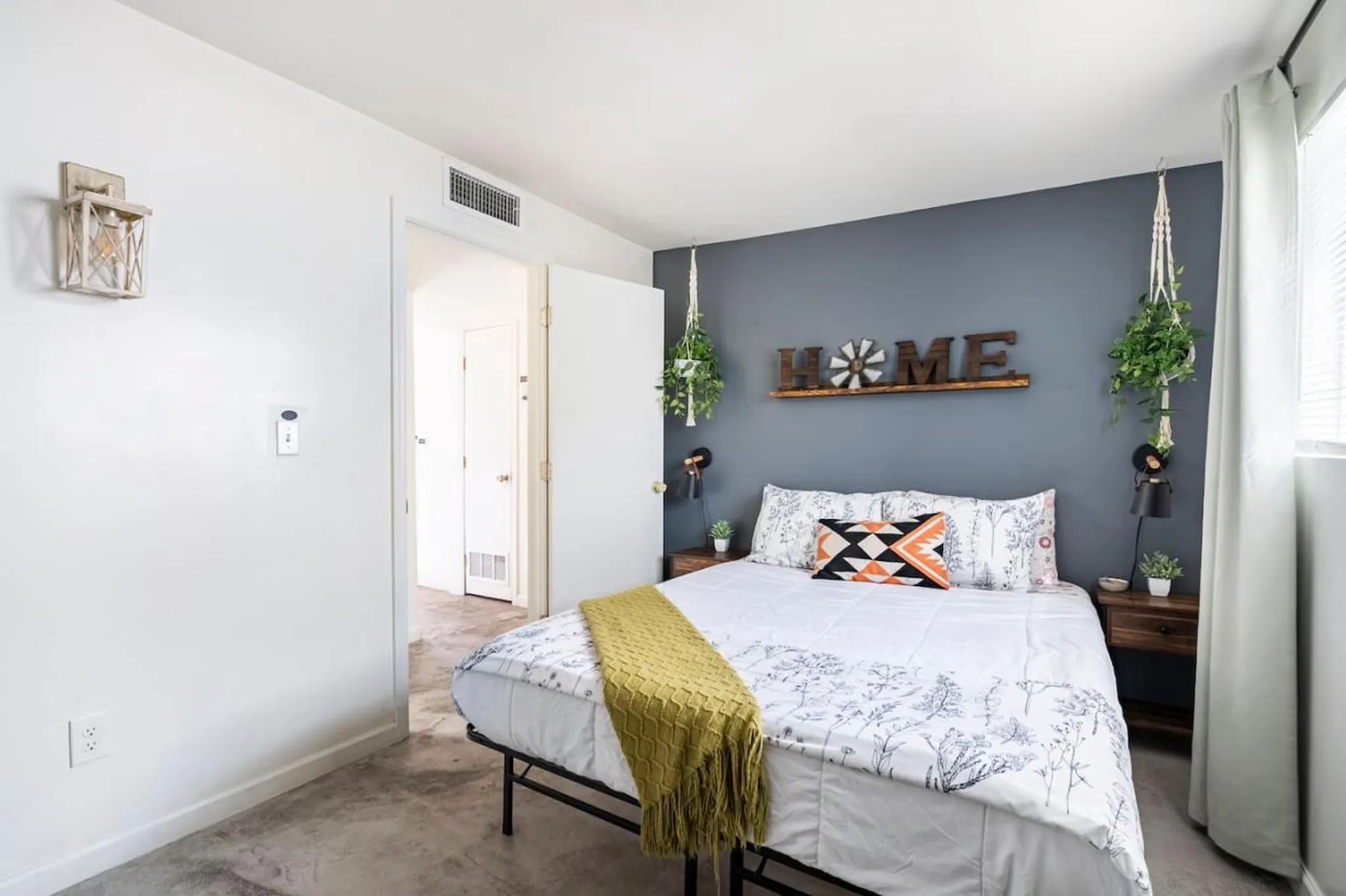 A bedroom with a bed, nightstand, and plants.