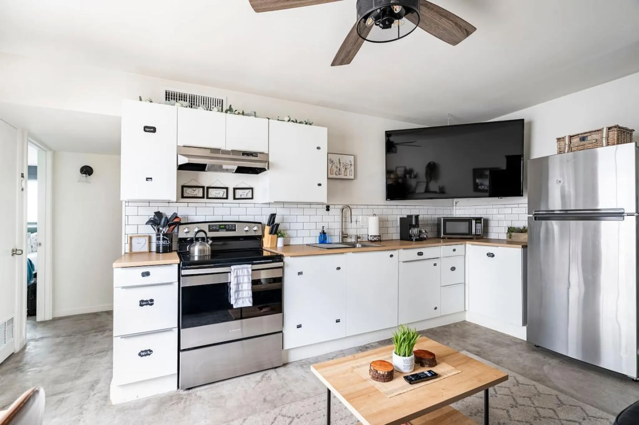 A modern kitchen with stainless steel appliances, white cabinets, and a TV mounted on the wall.