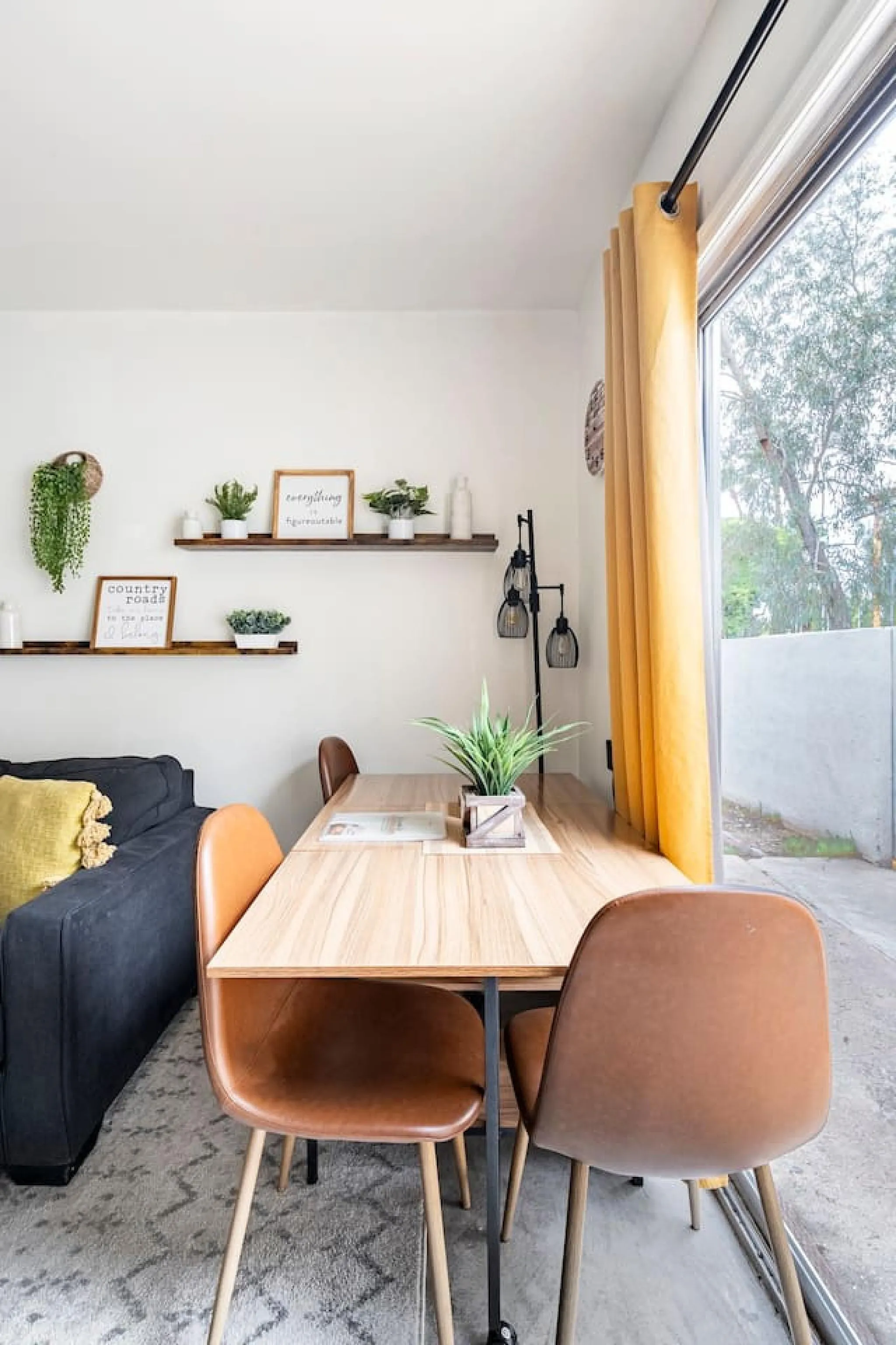 A dining room with a wooden table and chairs, facing a window with yellow curtains.