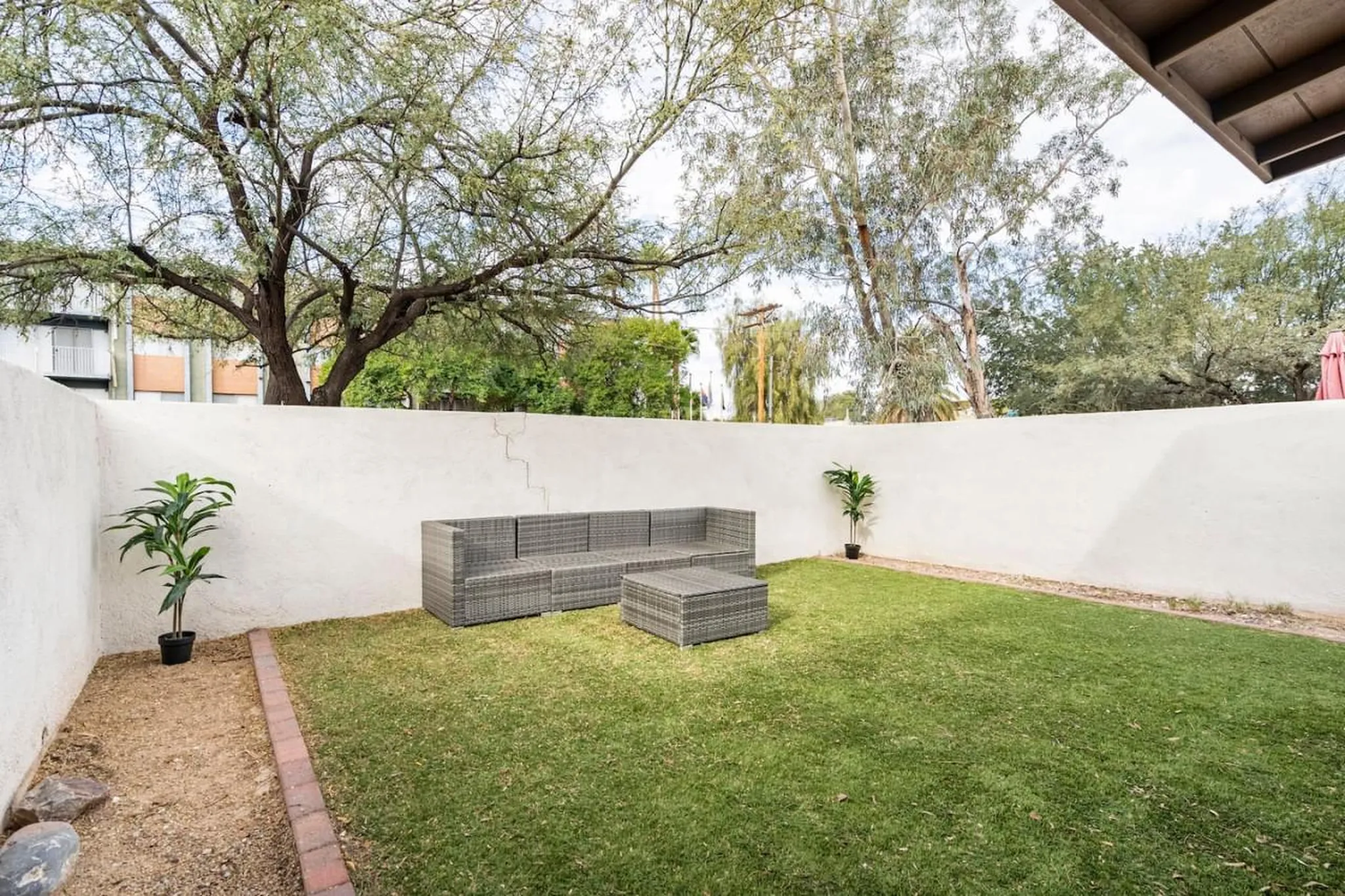 A spacious fenced-in backyard with a gray wicker couch and coffee table on a lawn.
