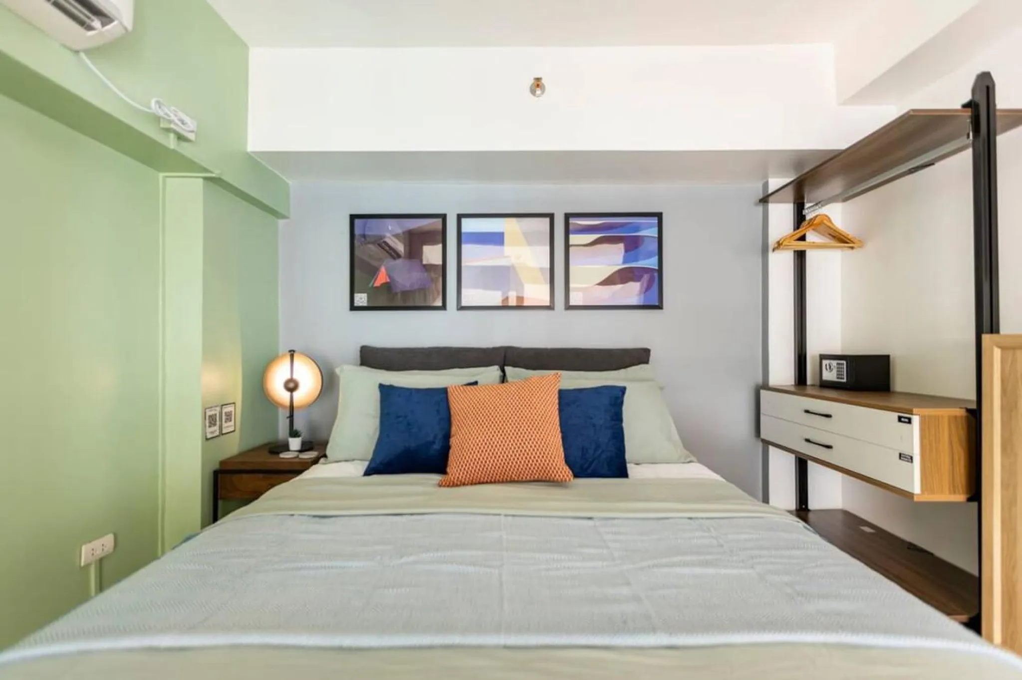 A bed in a bedroom with a safe and a clothes rack.