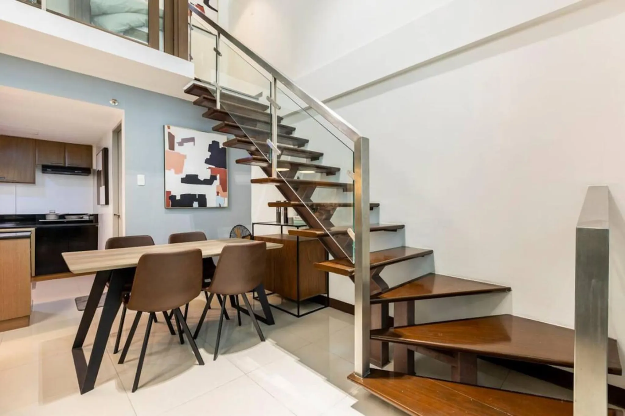 A dining area is set up next to a modern staircase with glass railings.