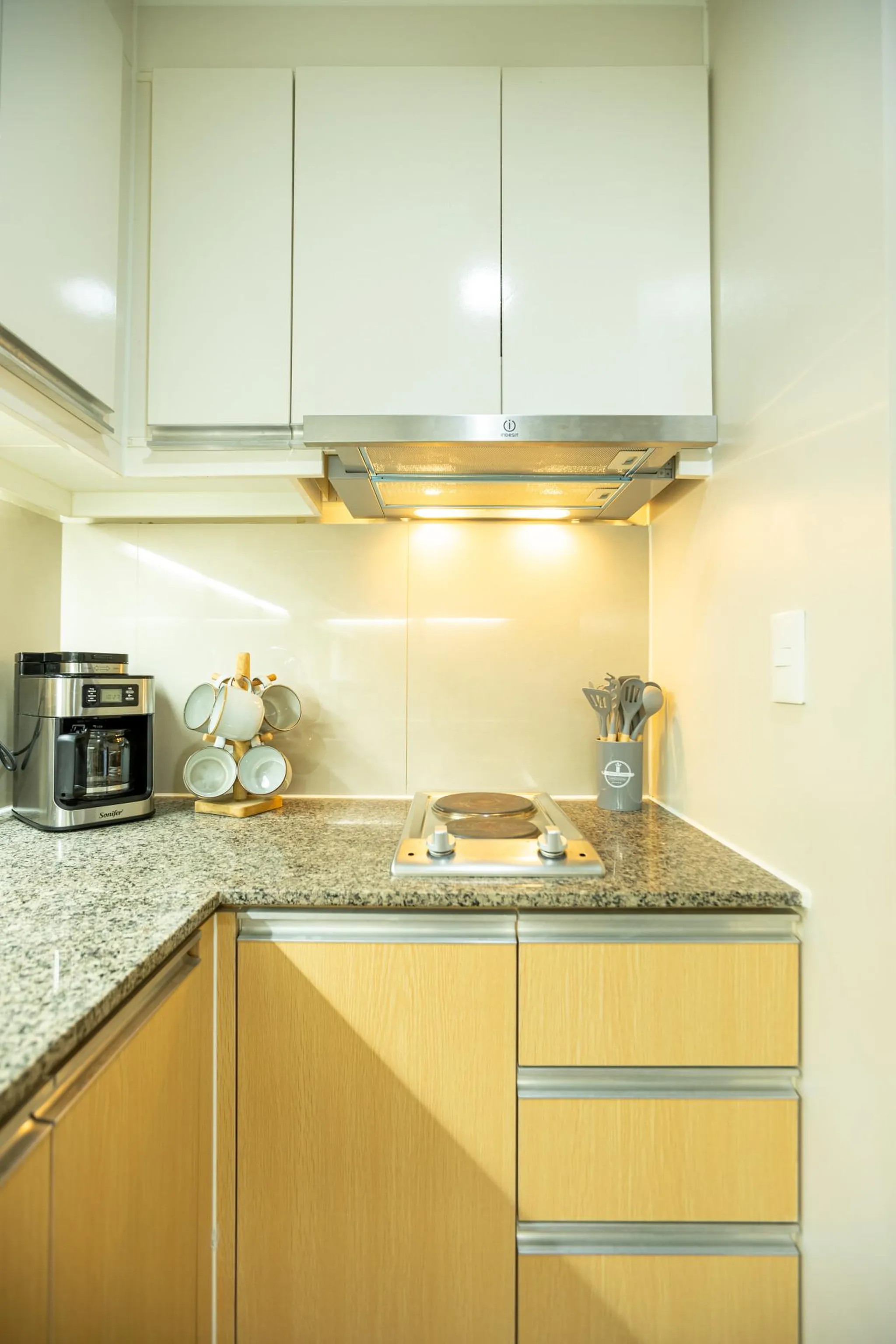 Kitchen with cabinets, coffee maker, cups on a tree, and a stovetop.