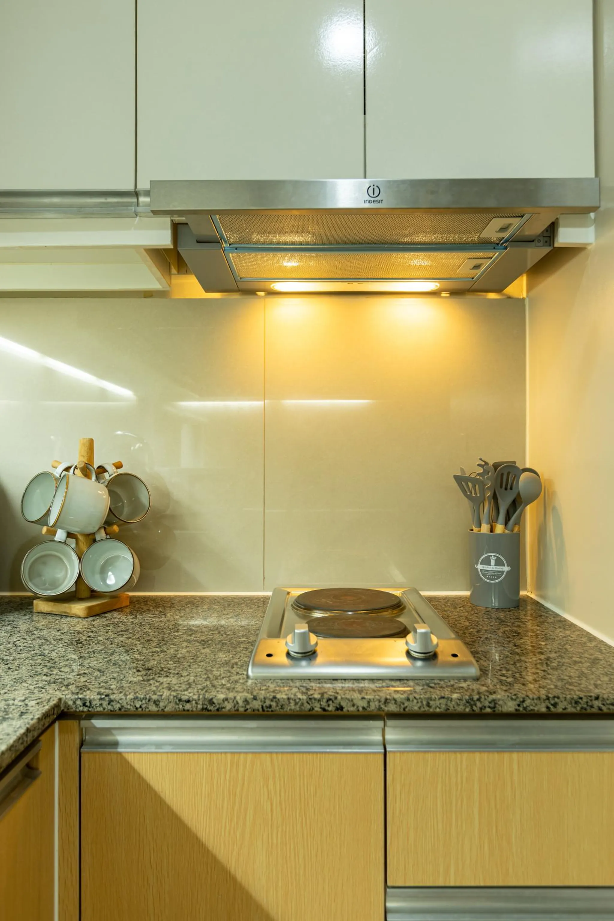 Kitchen with a stovetop, mugs, and utensils.