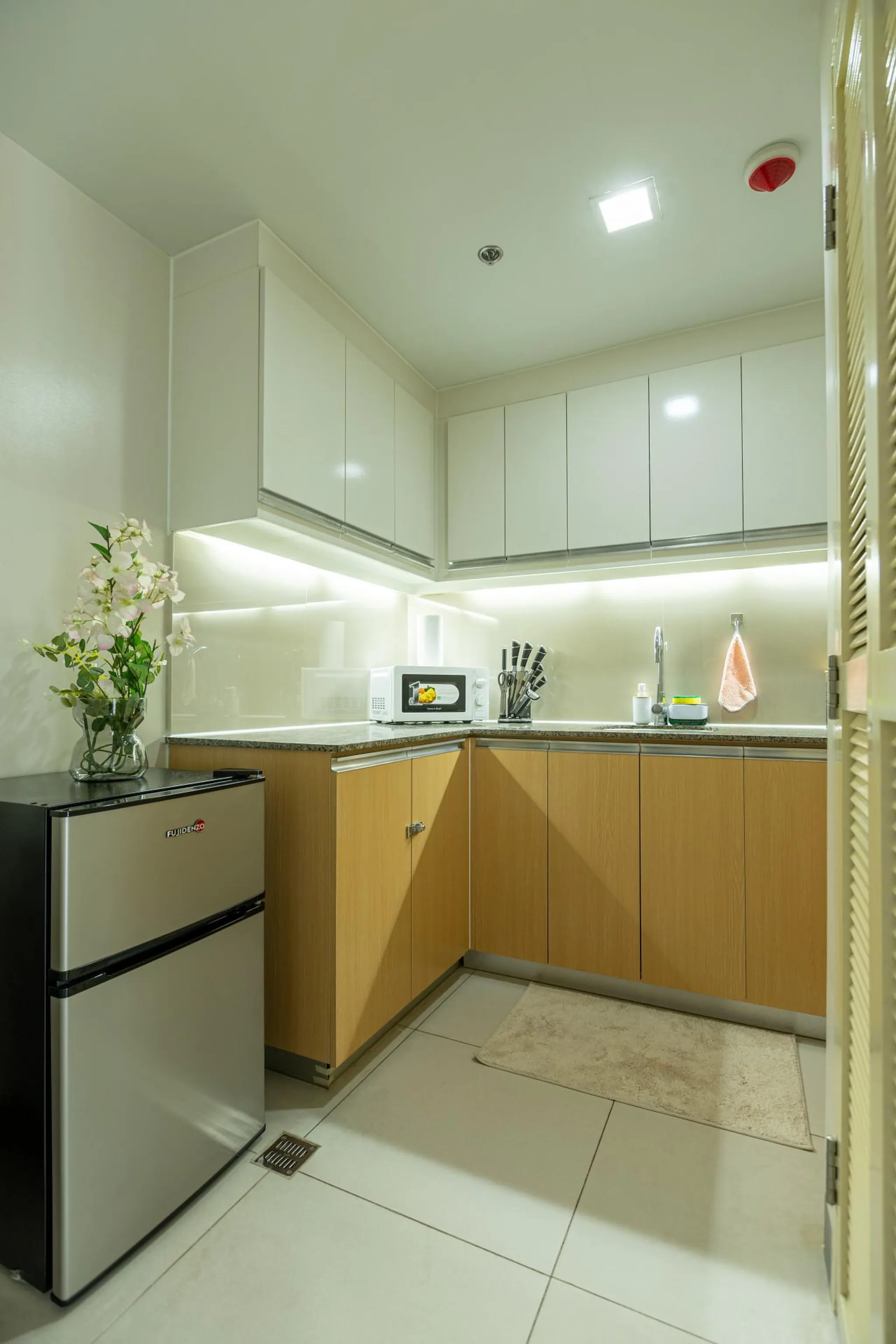 A modern kitchen with light wooden cabinets, white countertops, and a silver mini-fridge.
