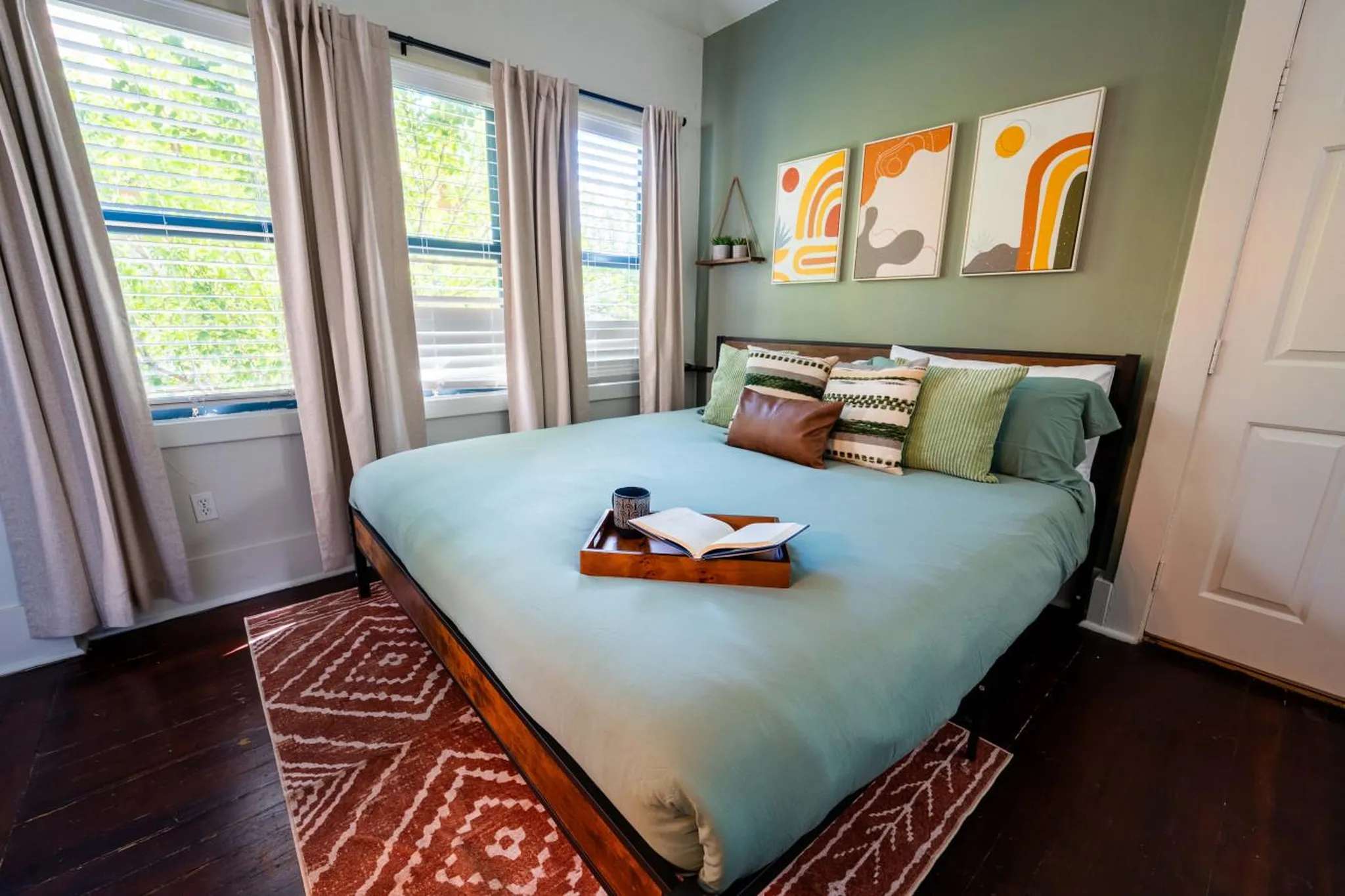 A bed with a teal comforter and decorative pillows sits in a bedroom.