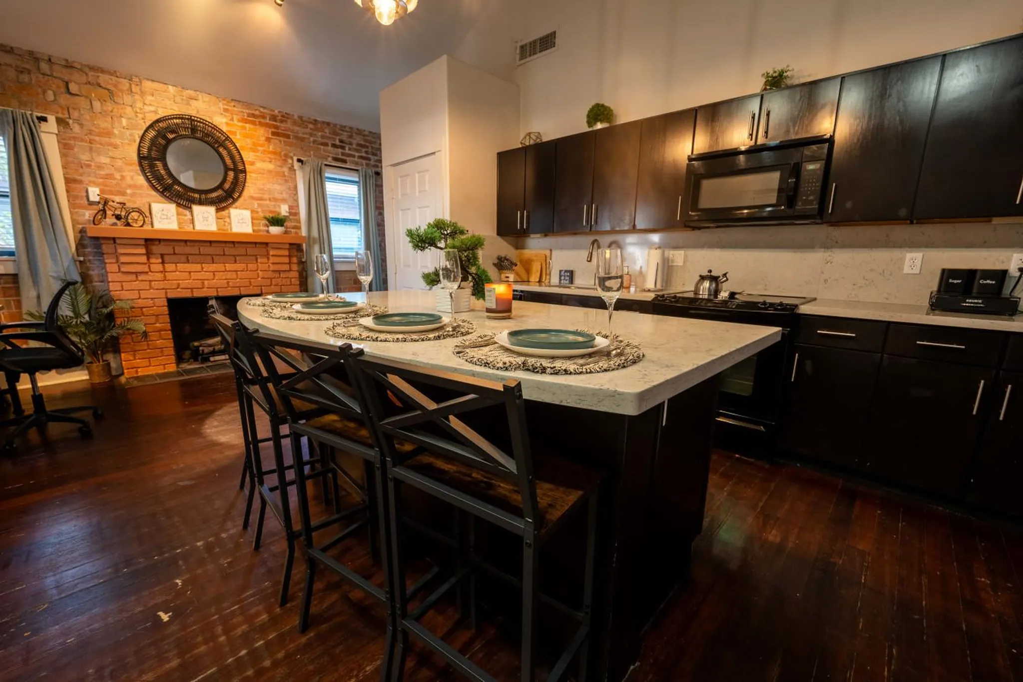 Kitchen and dining area with brick fireplace, island with bar stools, and dark cabinets.