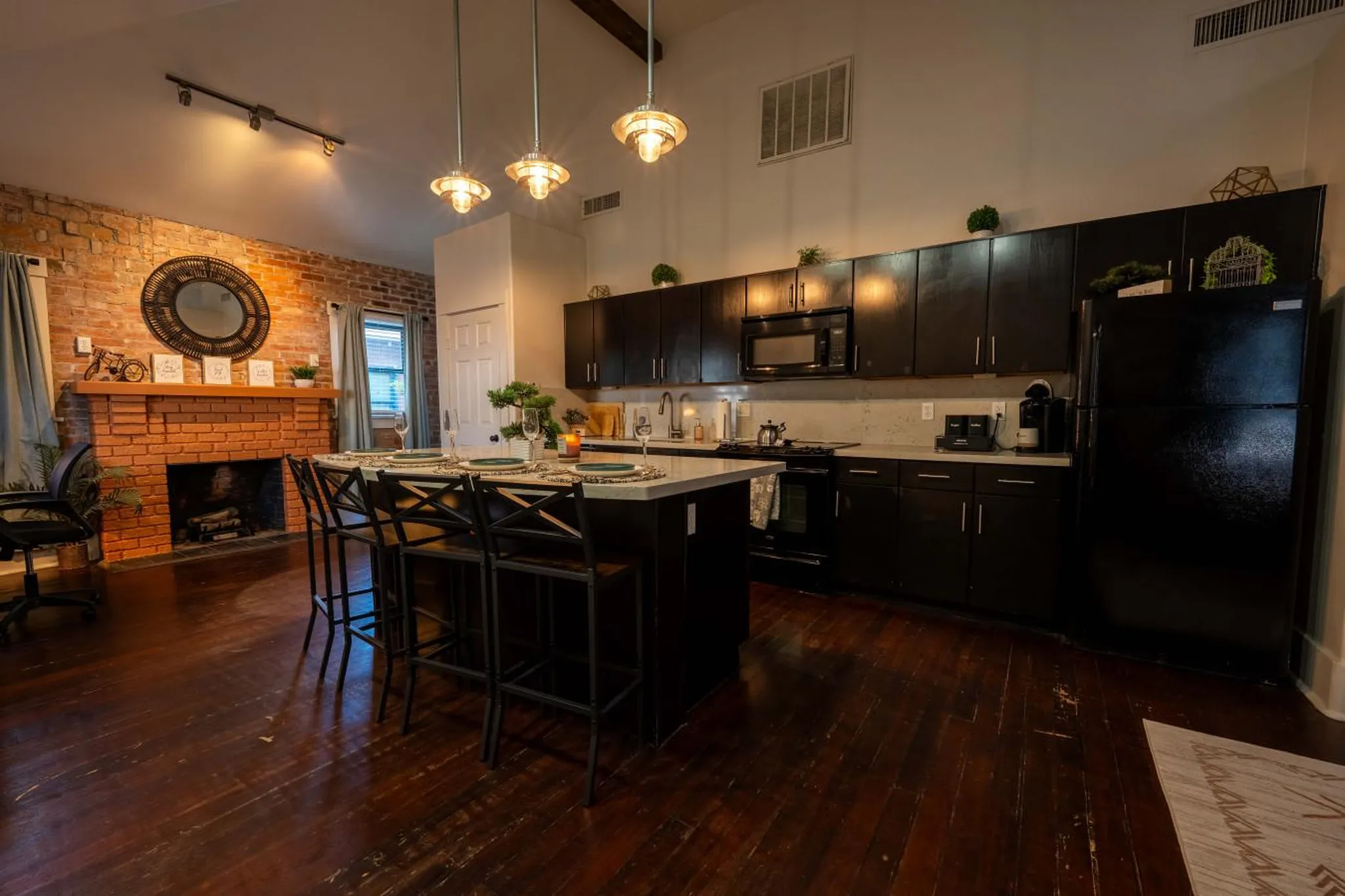 A black kitchen island with bar stools faces a kitchen with black cabinets and a black refrigerator.