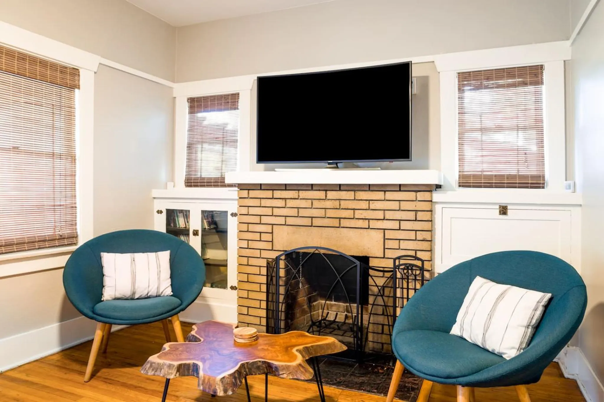 Two teal chairs and a live-edge coffee table in front of a brick fireplace with a TV above.