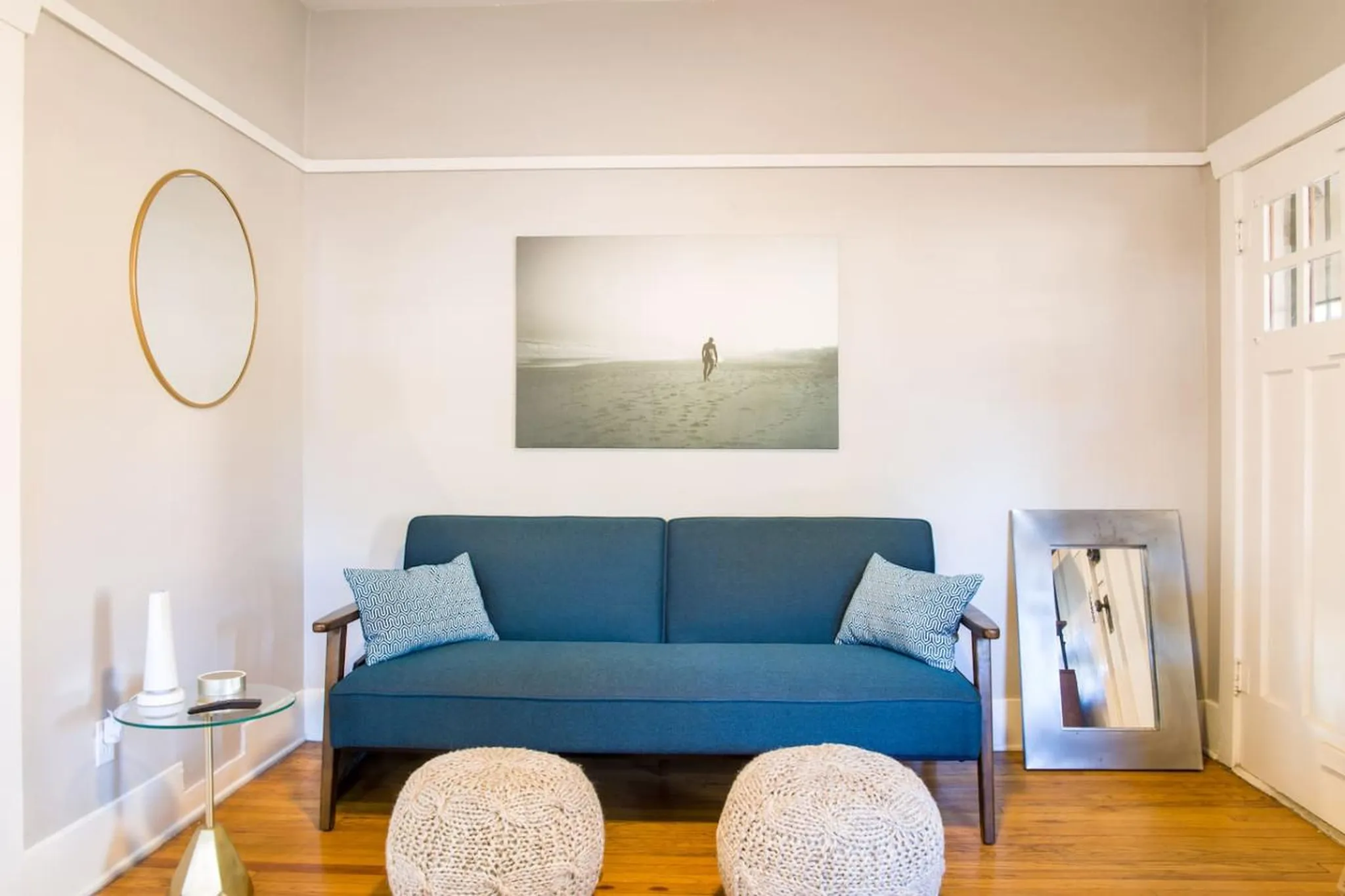 A blue couch with patterned pillows sits in a living room with a beach scene artwork.