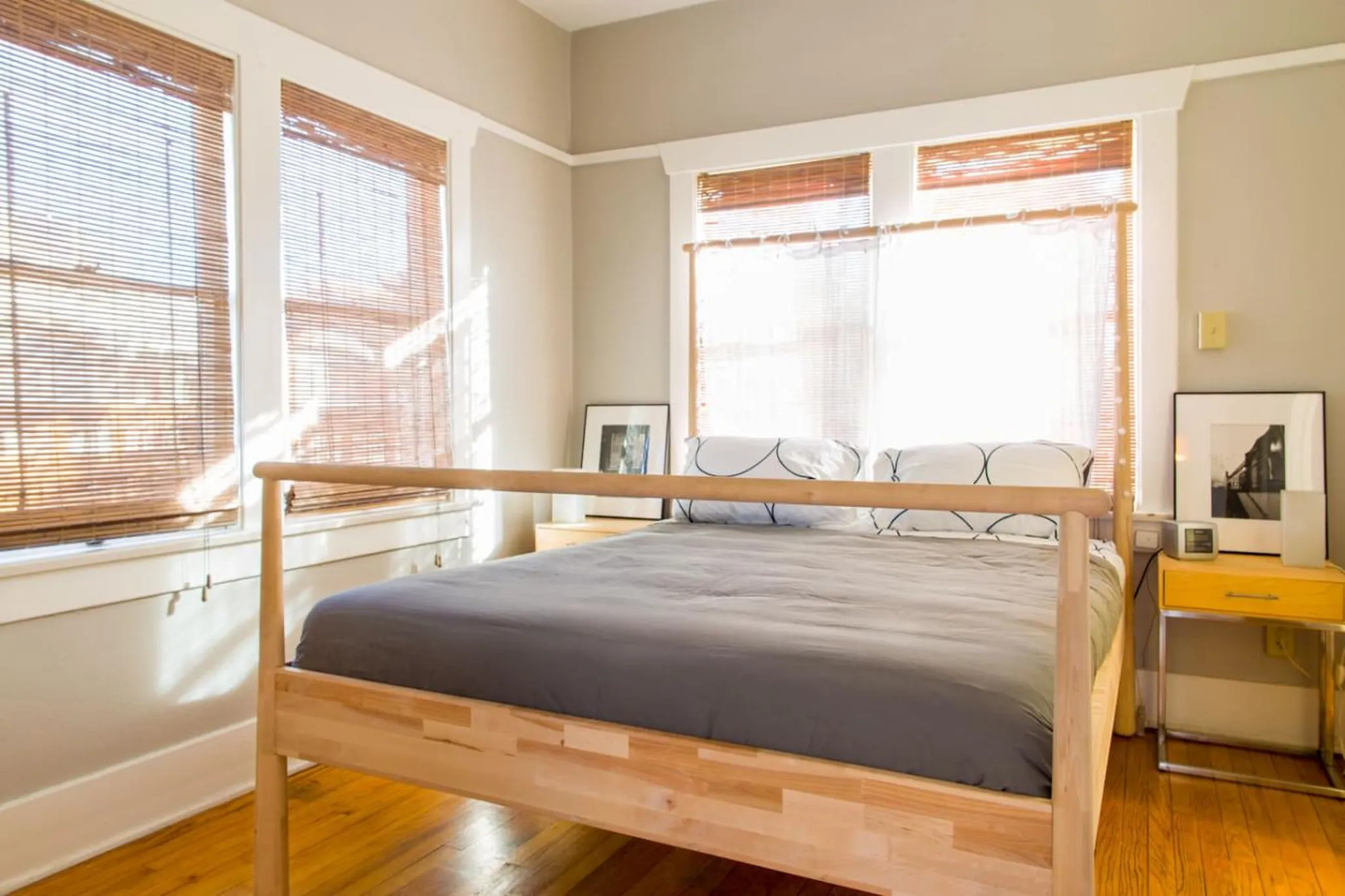 A modern bedroom with a wooden bed frame and two windows with bamboo blinds.