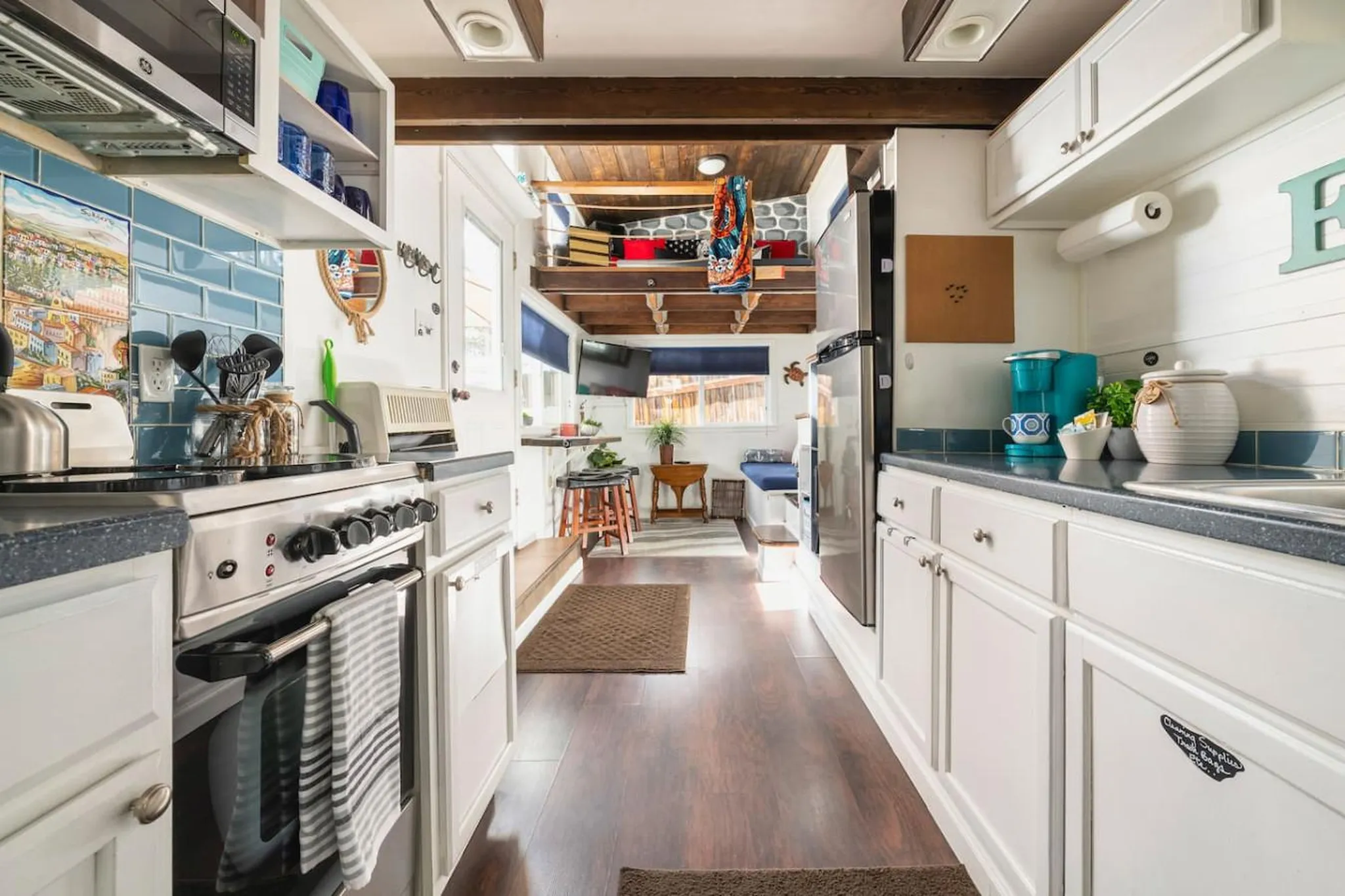 A tiny home kitchen with a stove, cabinets, and a loft bedroom above.