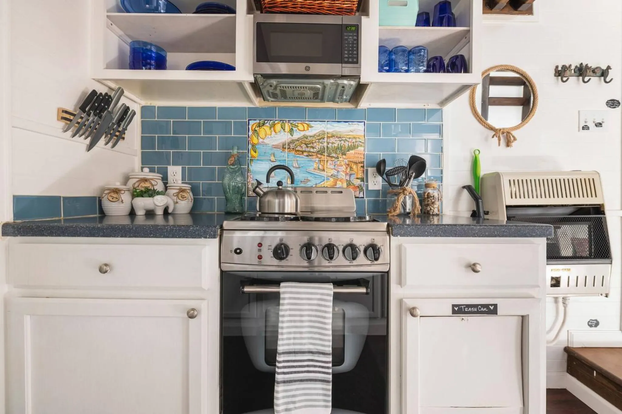 A compact kitchen features a stove, microwave, and blue subway tile backsplash.