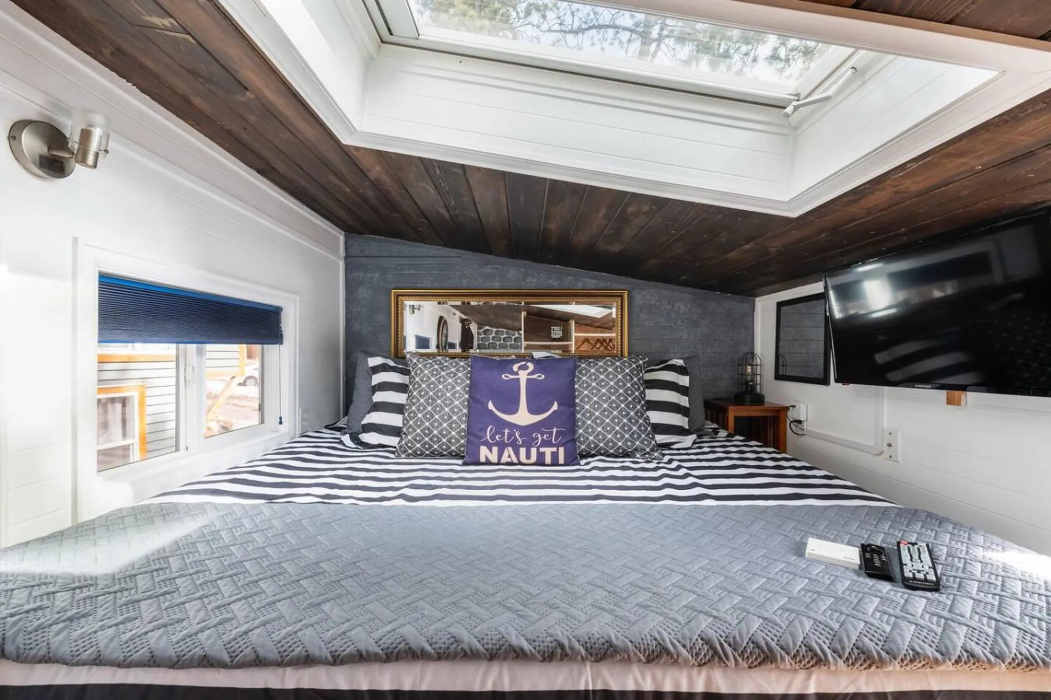 A queen-sized bed with nautical-themed pillows sits under a skylight.