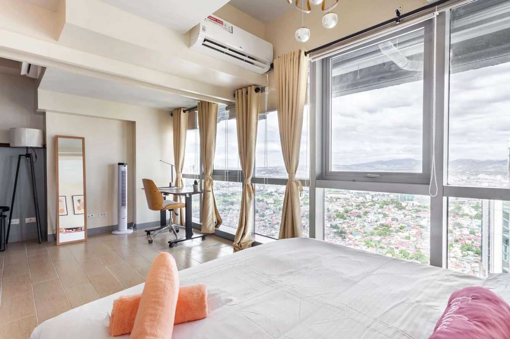 A bedroom with a bed, desk, and large windows overlooking a city.