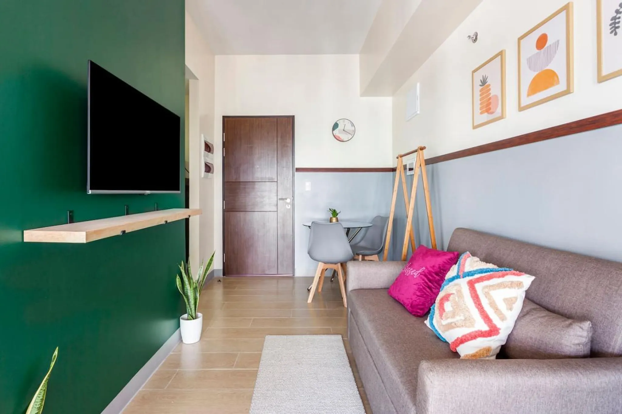 A modern living room with a couch, dining set, and TV on a green wall.