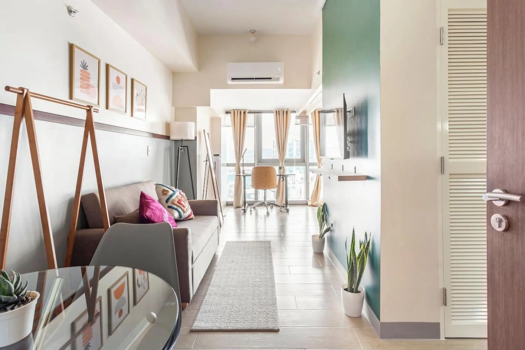 A modern apartment living room with a sofa, desk, and plants.