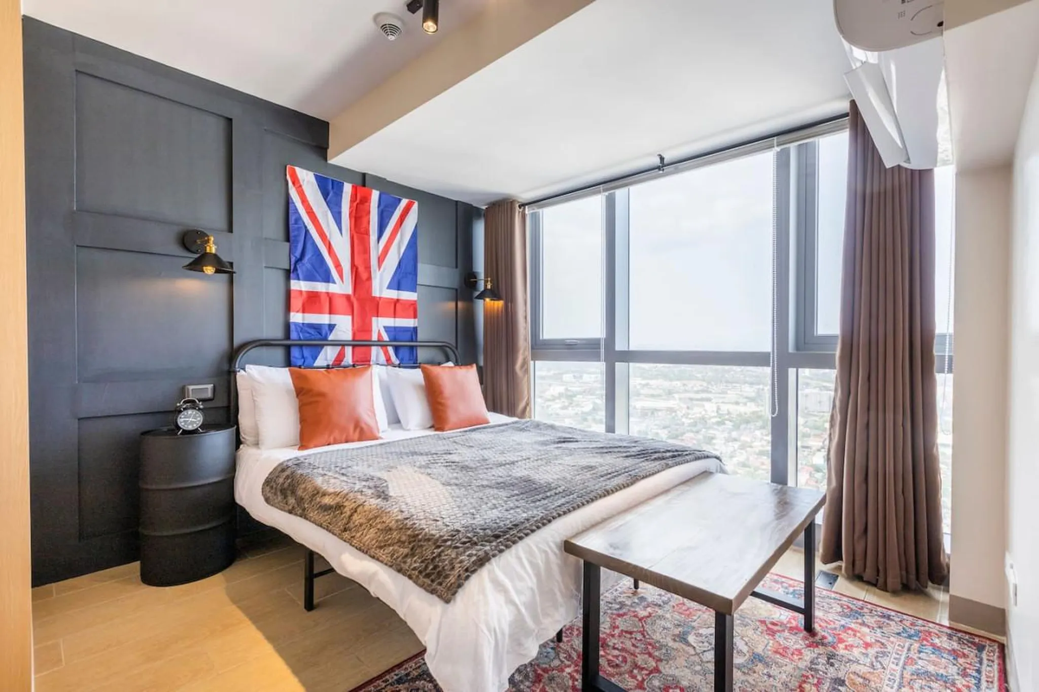 A bedroom with a Union Jack flag and a large window with a city view.