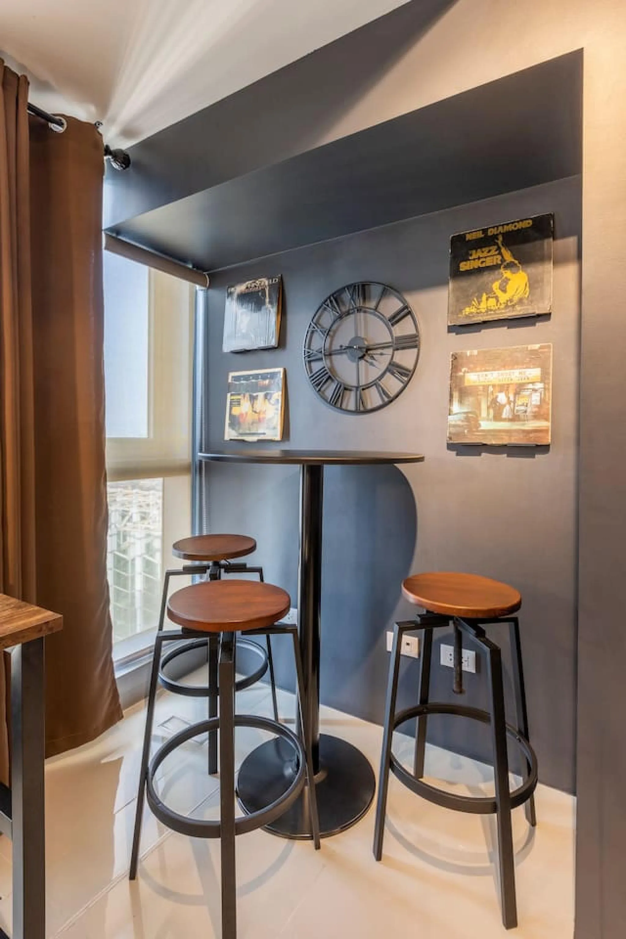 A high-top table with three stools is positioned in front of a wall adorned with album covers and a 