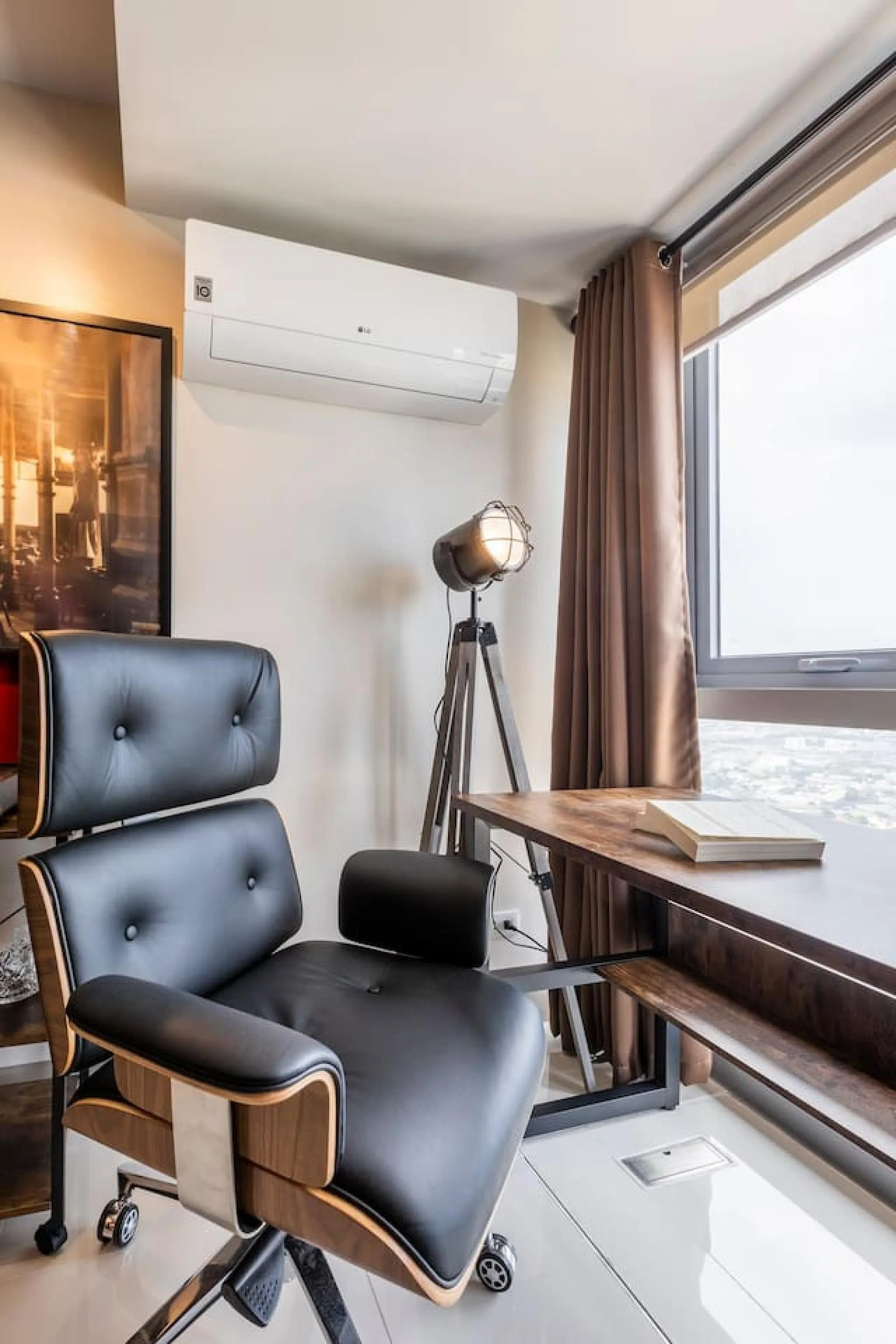 An office chair and desk by a window with an air conditioner on the wall.