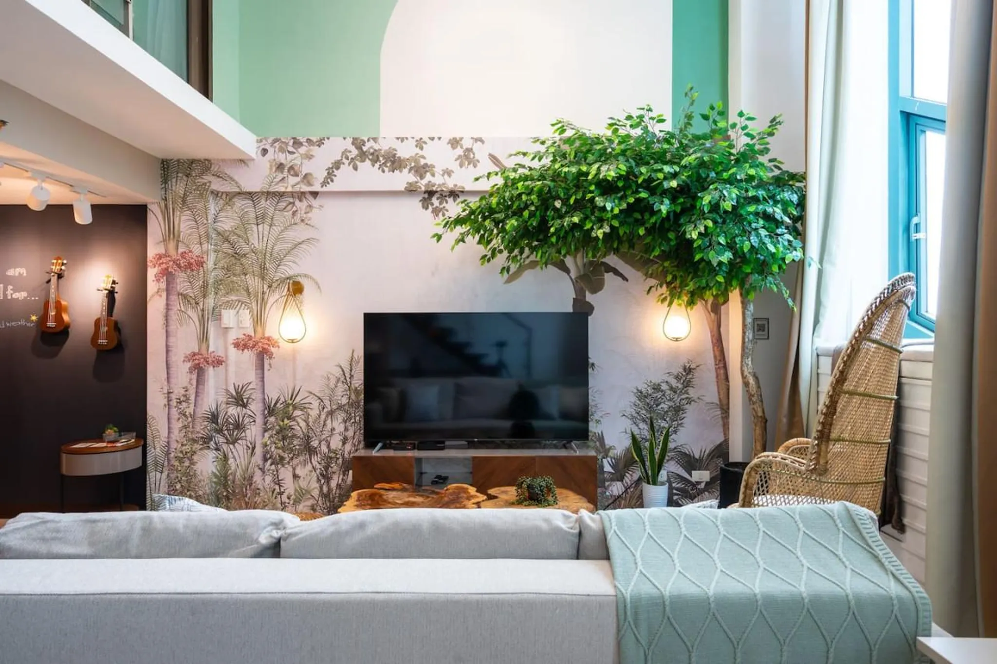 A living room with a large television, a sofa, and a wicker chair.