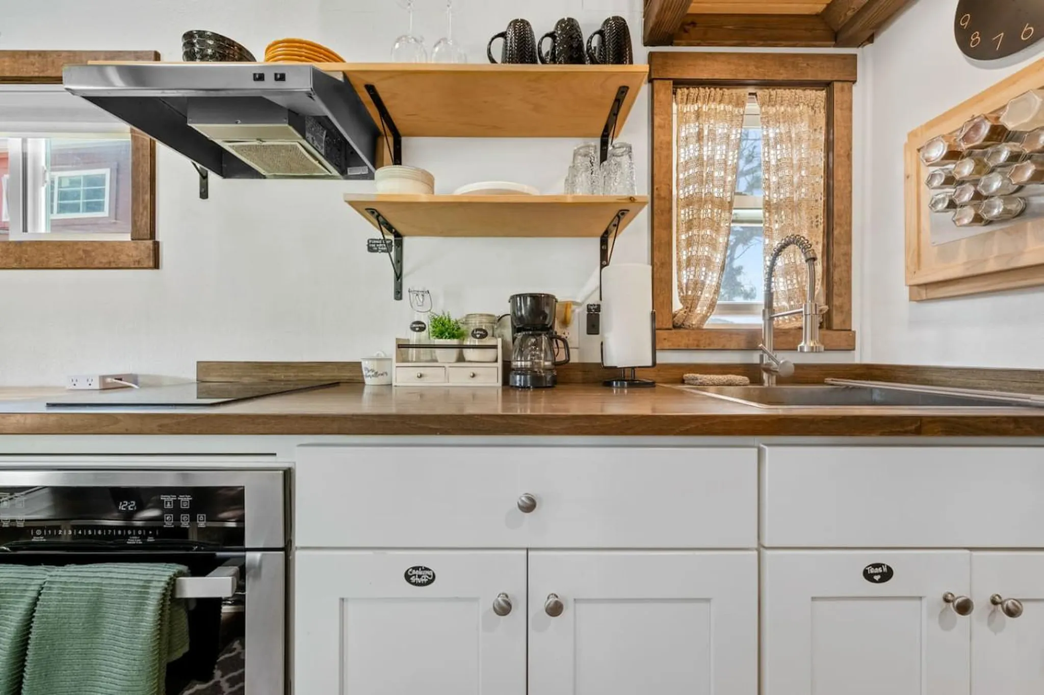 Kitchen with white cabinets, stainless steel oven, wood countertops, and shelves with mugs and plate